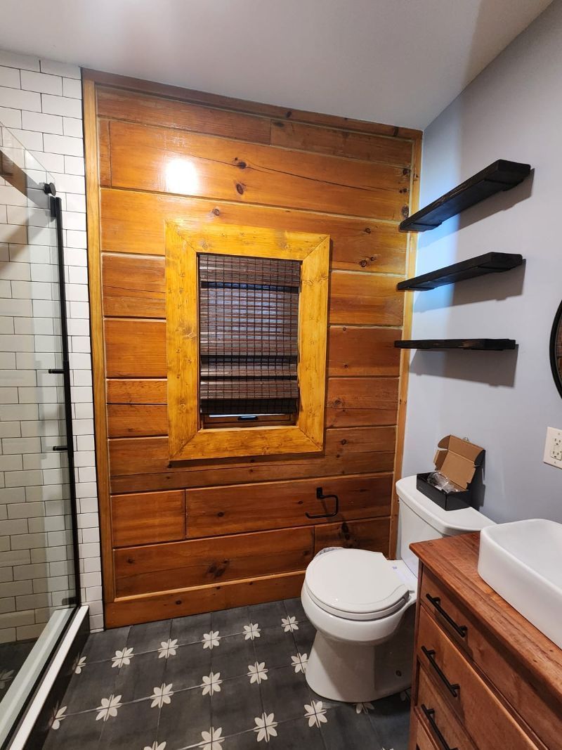 A bathroom with a toilet , sink , mirror and wooden wall.