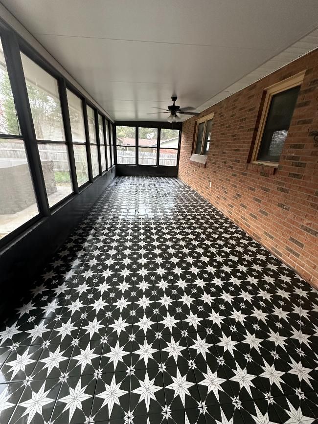 A screened in porch with black and white tiles and a ceiling fan.