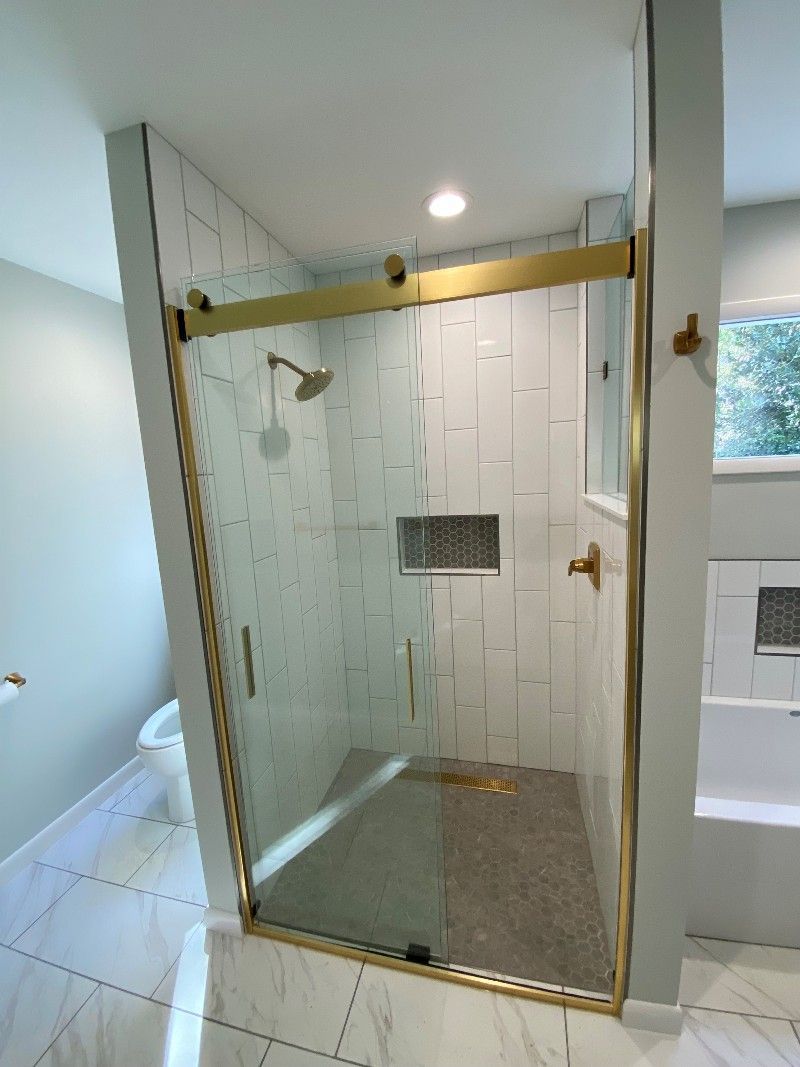 A bathroom with a walk in shower with a gold frame.