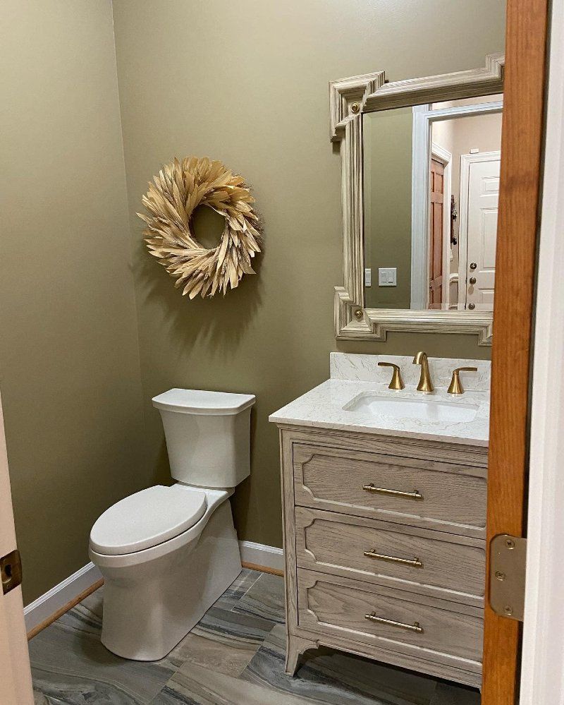 A bathroom with a toilet , sink , mirror and wreath on the wall.