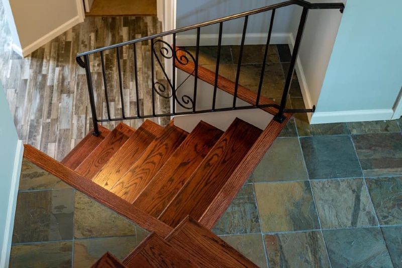A wooden staircase with a metal railing and a tiled floor