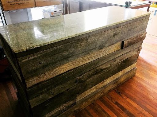 A wooden counter with a granite counter top is sitting on a wooden floor.