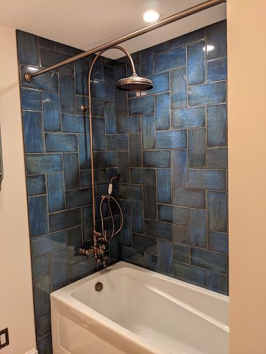 A bathroom with blue tiles and a bathtub with a shower head.