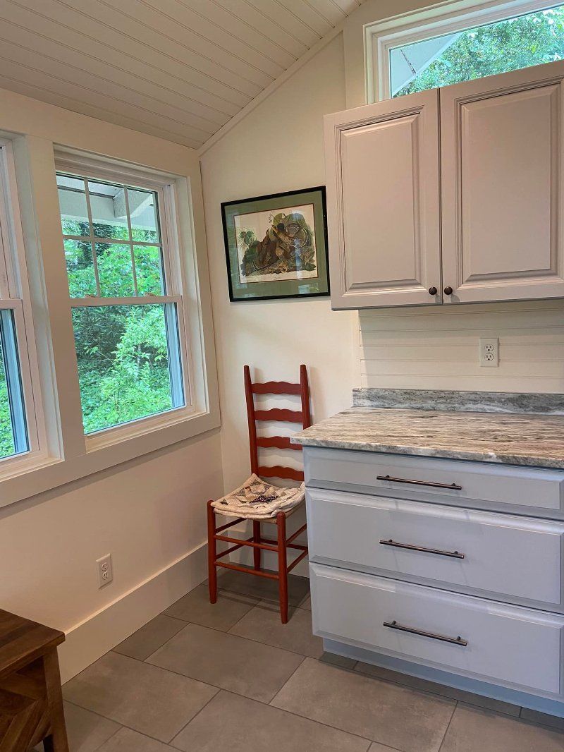 A kitchen with white cabinets , granite counter tops , and a red chair.