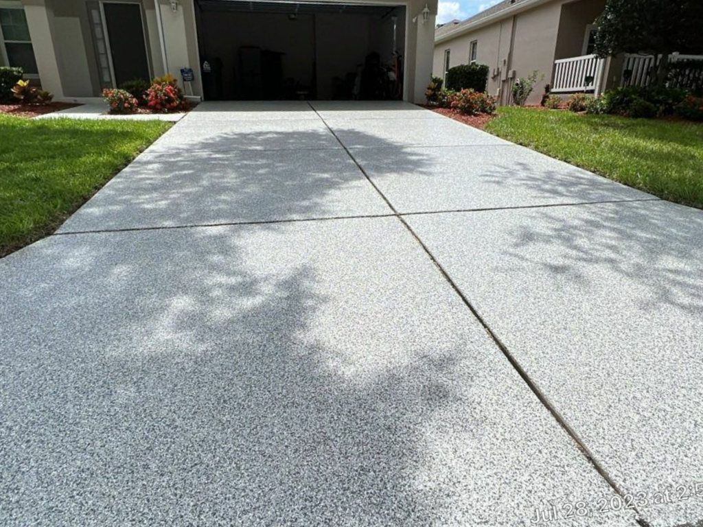 Concrete driveway with decorative gray speckled coating, leading to a garage entrance, flanked by grass.