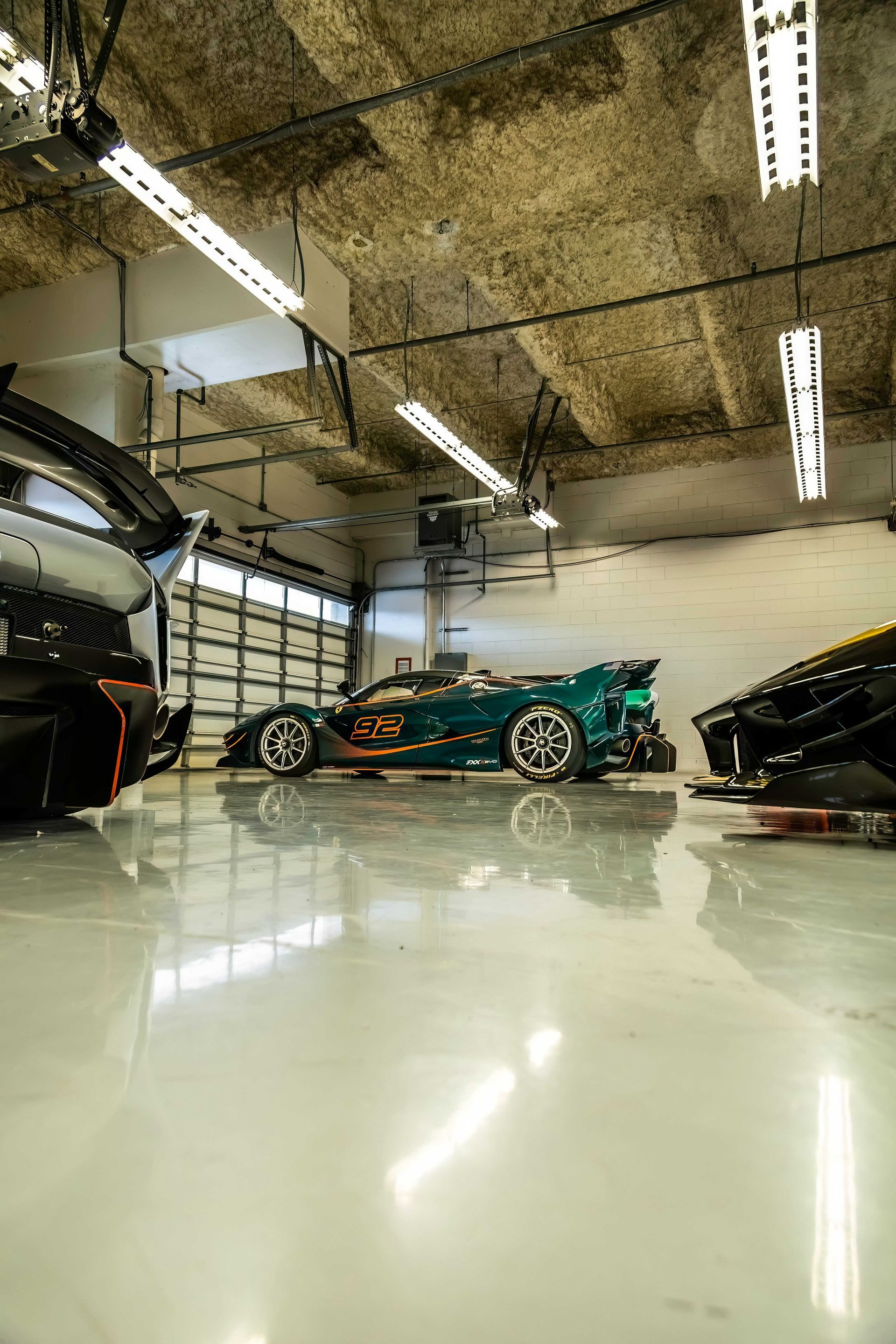 Shiny garage with high-end sports cars. Green car center stage, black car left, yellow car right. White floor and ceiling lights.