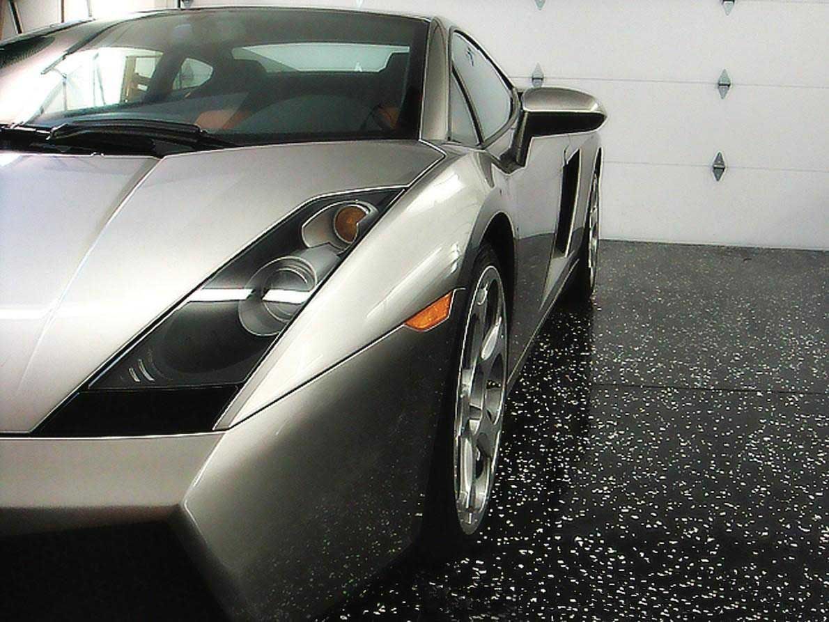 Silver Lamborghini parked in a garage with a speckled black floor.