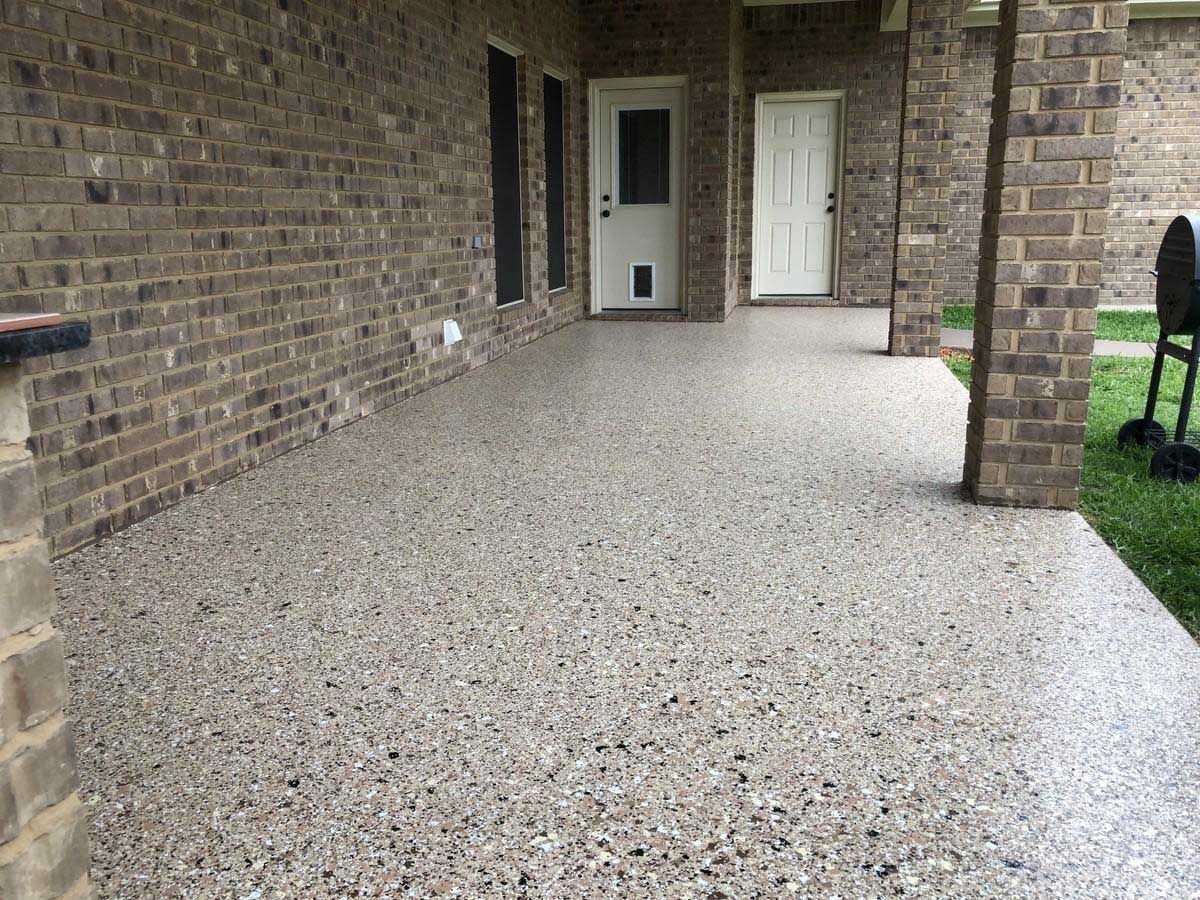 Concrete patio with exposed aggregate, brick walls and pillars, and two white doors.