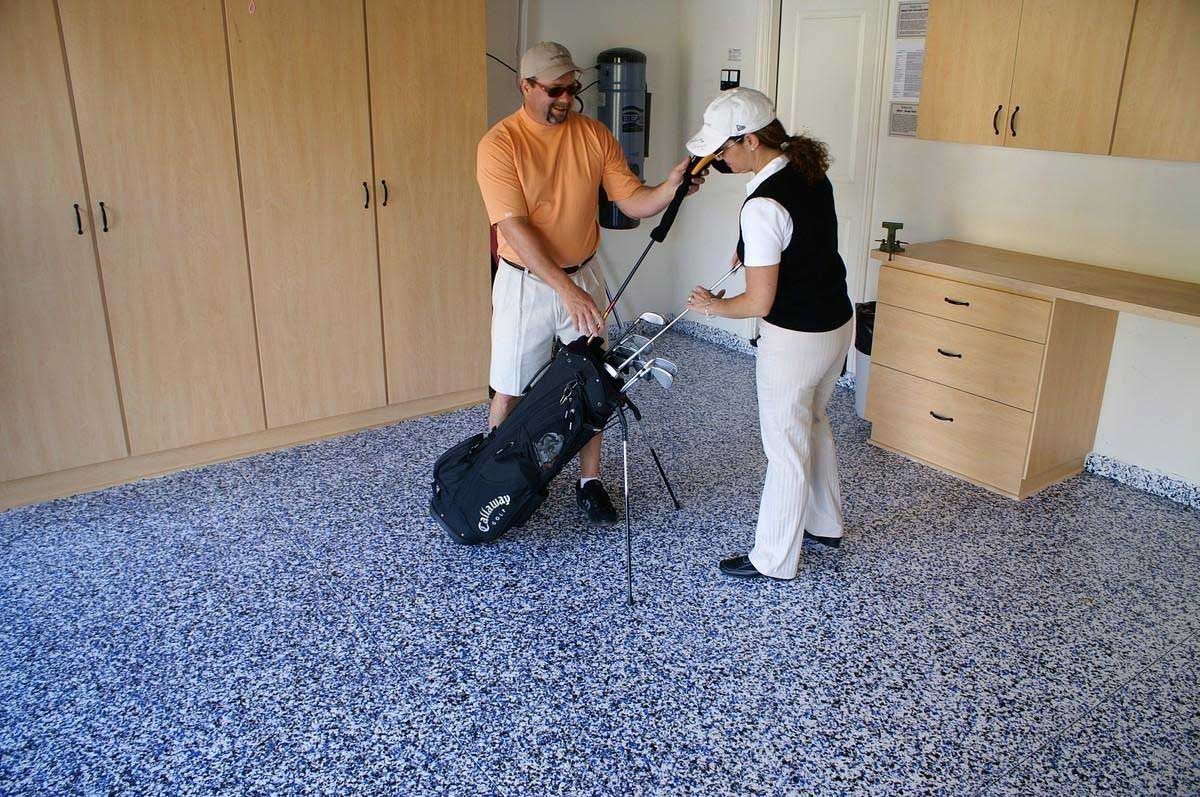 Man and woman in a garage with golf bag and clubs on blue speckled floor, looking at the clubs.