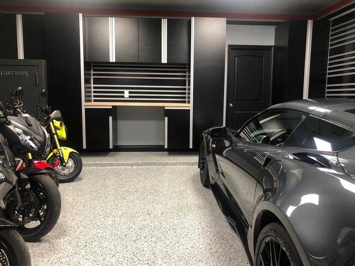 Garage with black cabinets, work area, motorcycles, and a gray sports car.