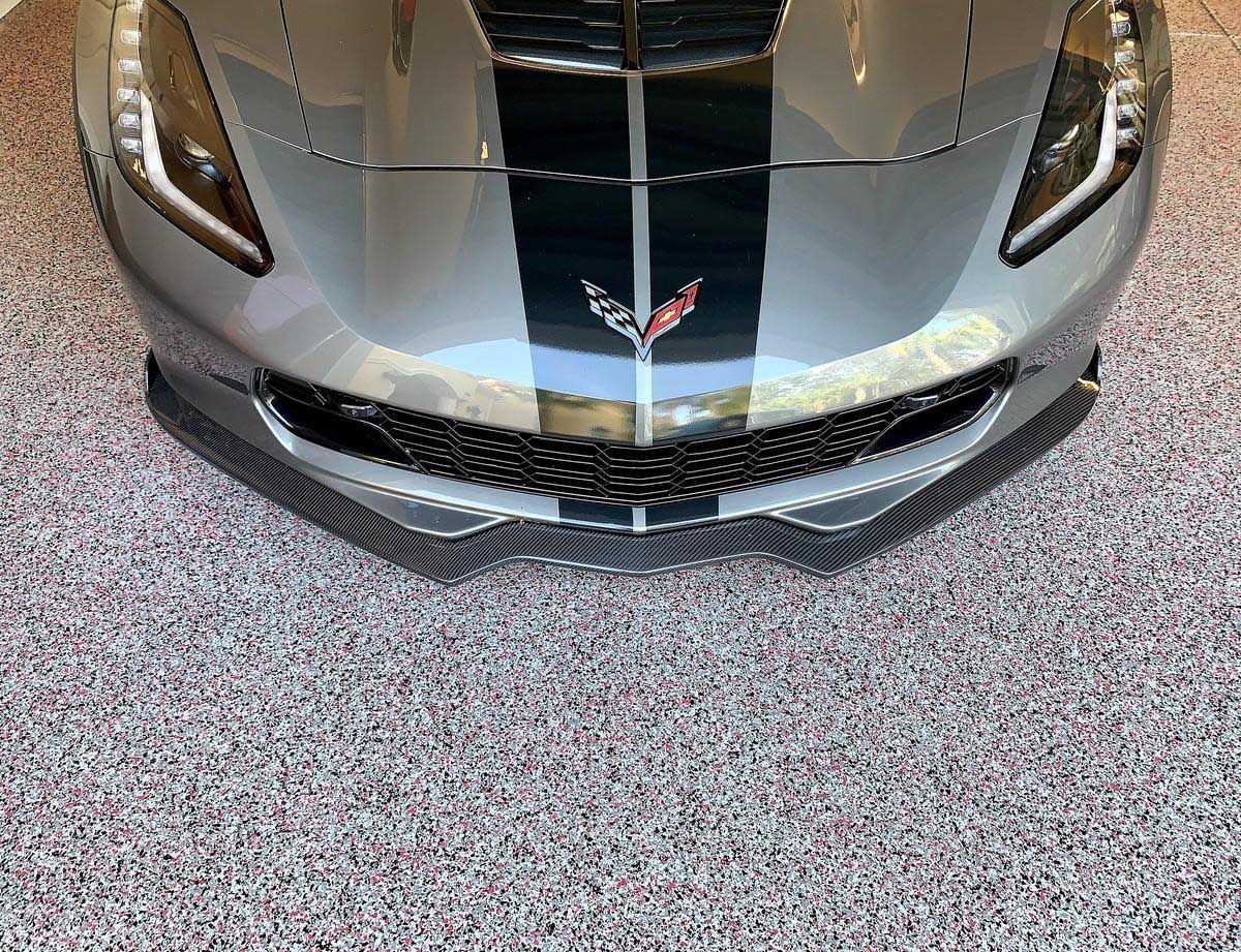 Gray Chevrolet Corvette with black racing stripes and red emblem on a speckled floor.