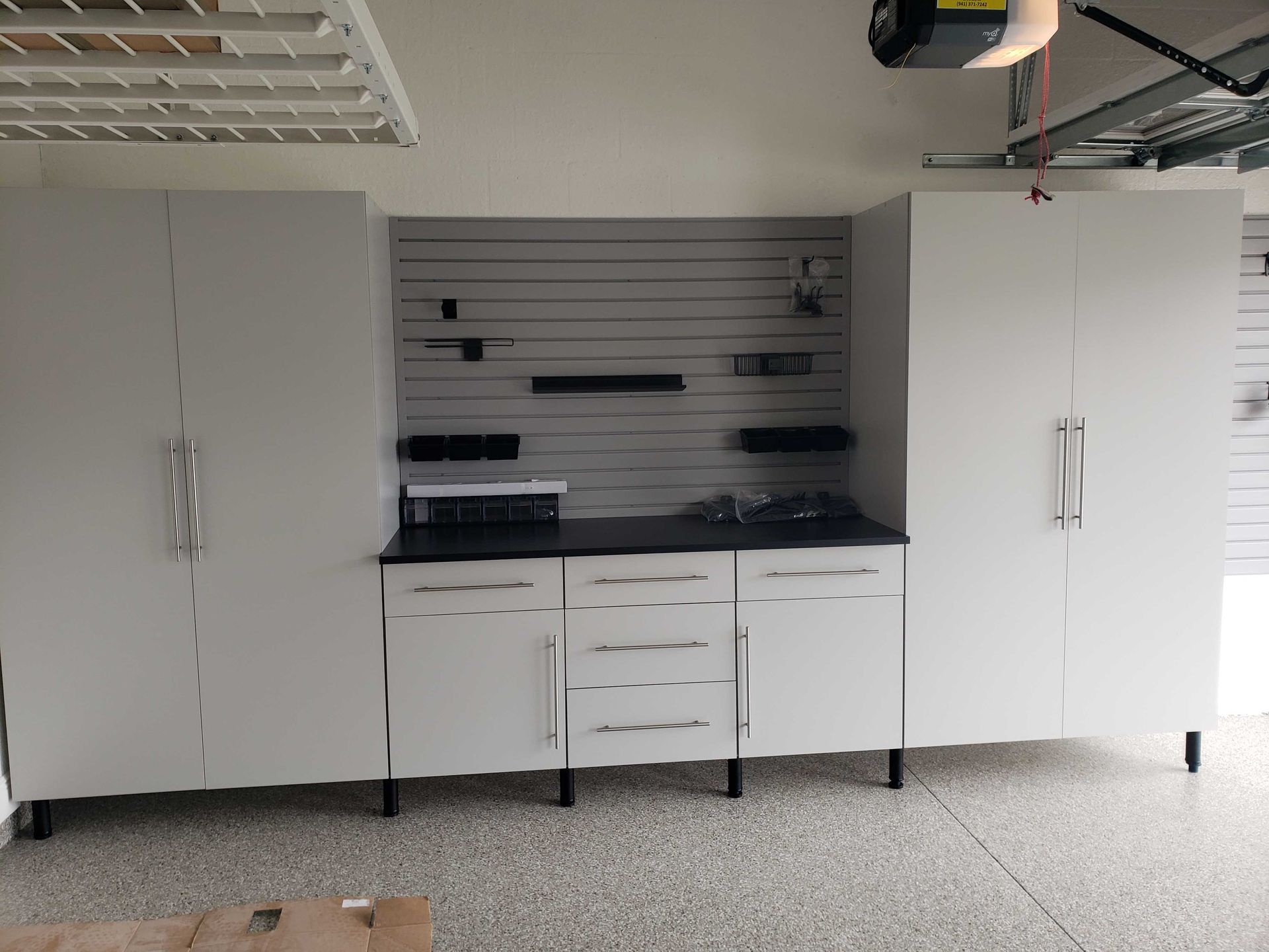 White garage storage cabinets with a workbench and gray slatwall.