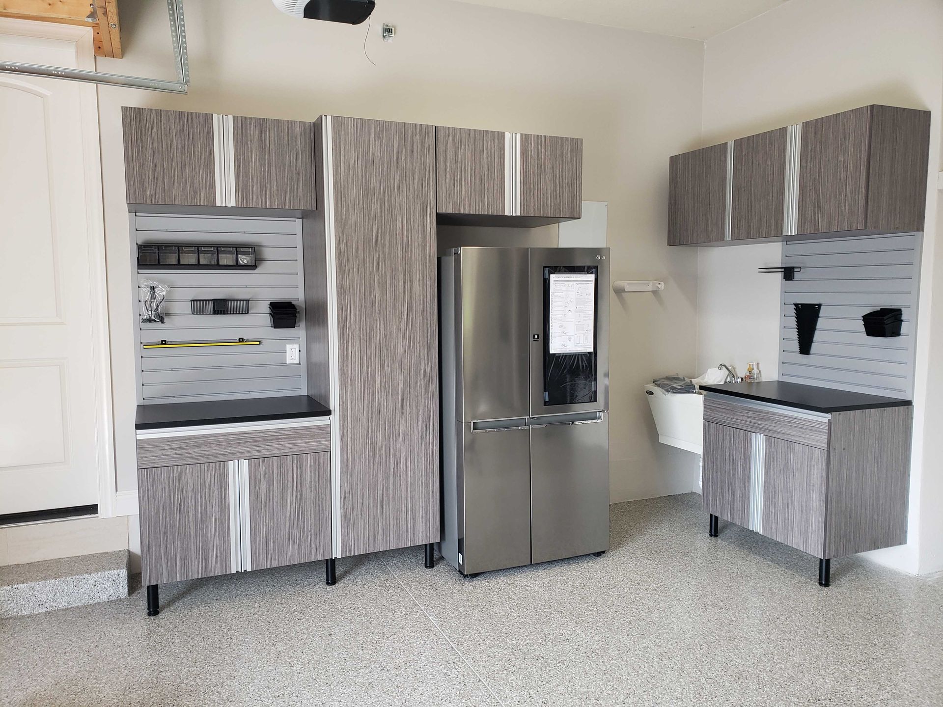 Garage with gray storage cabinets and a stainless steel refrigerator.