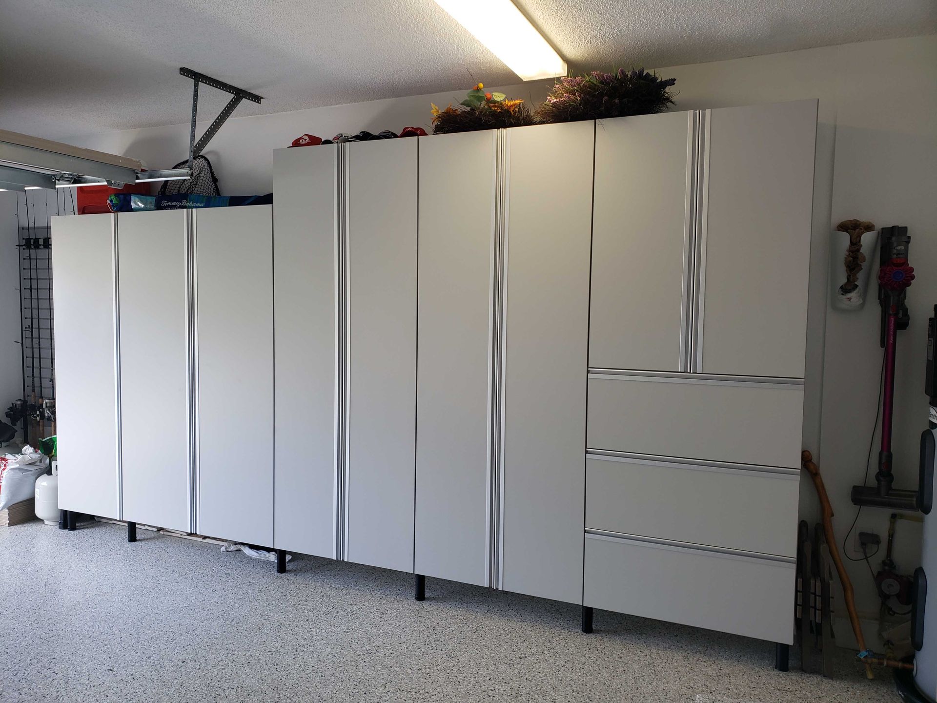 White storage cabinets line a garage wall, with wavy door designs and a vacuum on the right.