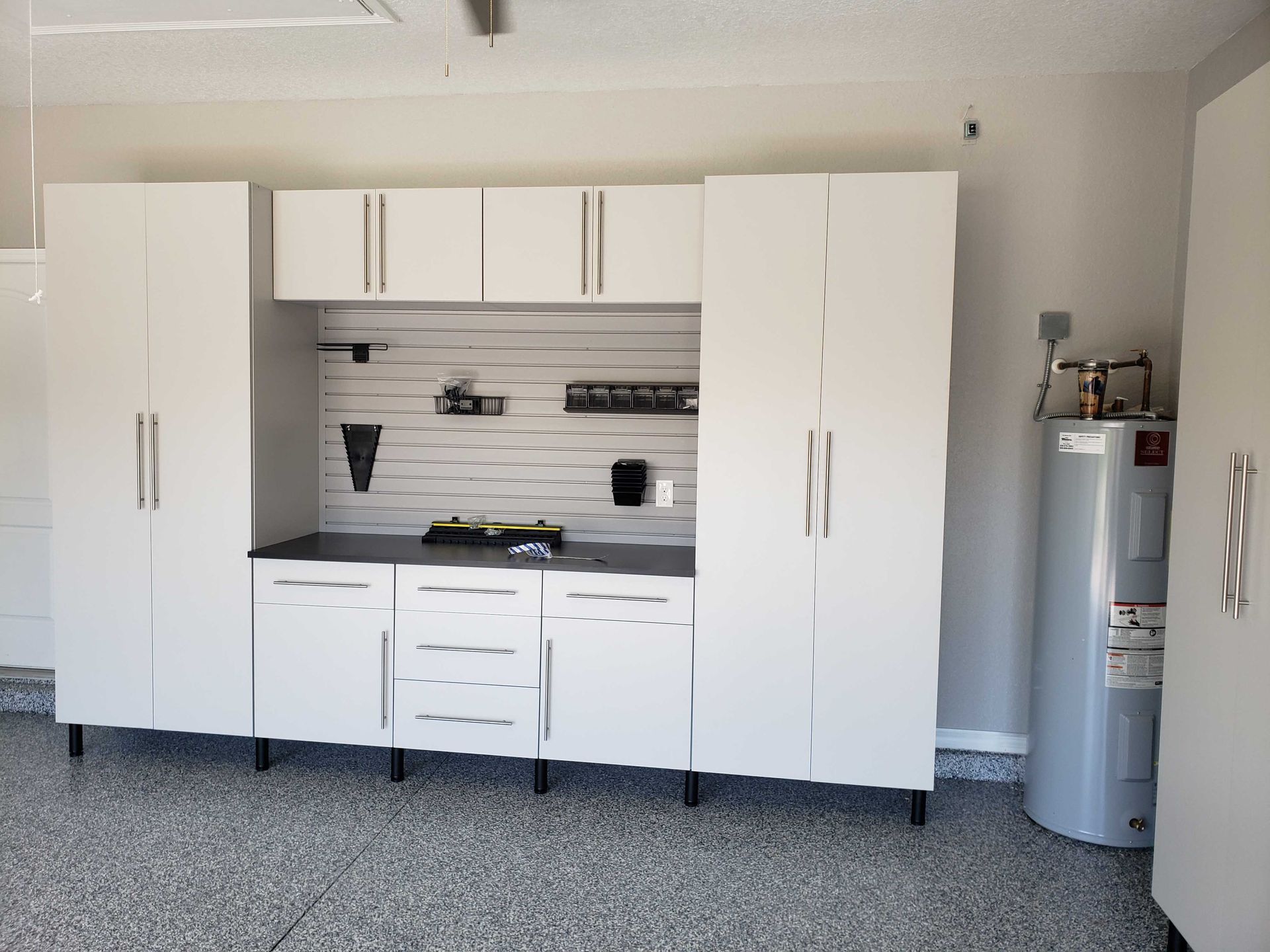 White garage storage cabinets with a workbench and water heater.