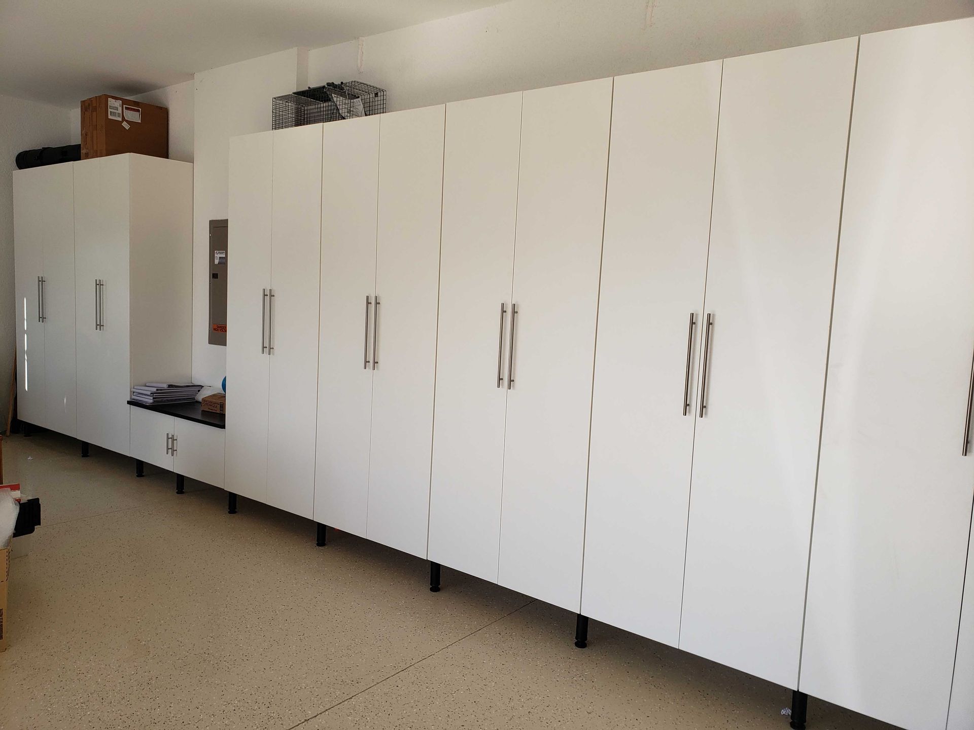 White garage cabinets with metal handles and black legs against a white wall.