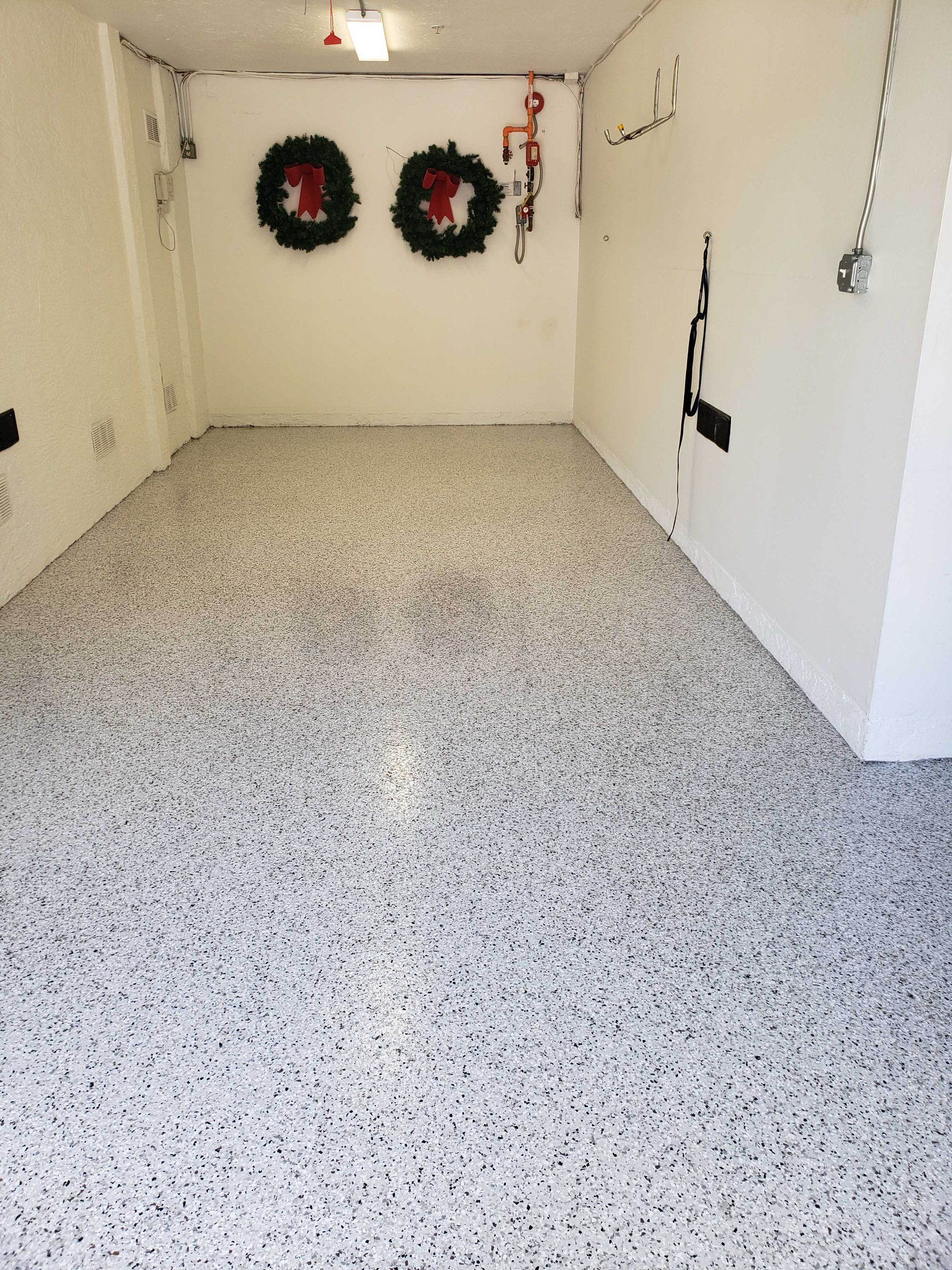 Garage with speckled floor, white walls, two wreaths, and various electrical fixtures.
