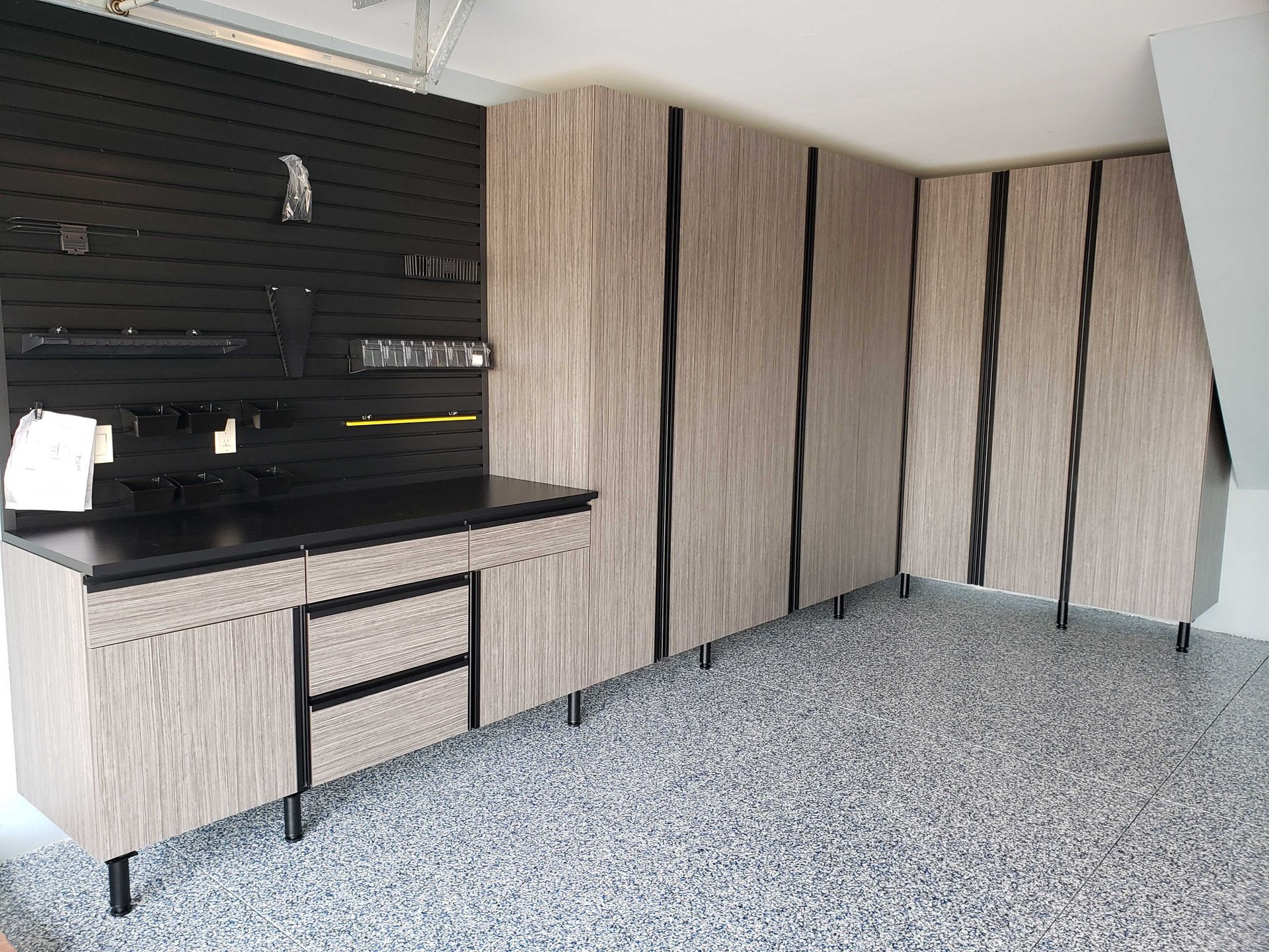Garage with wooden cabinets, black countertop, and speckled gray floor.