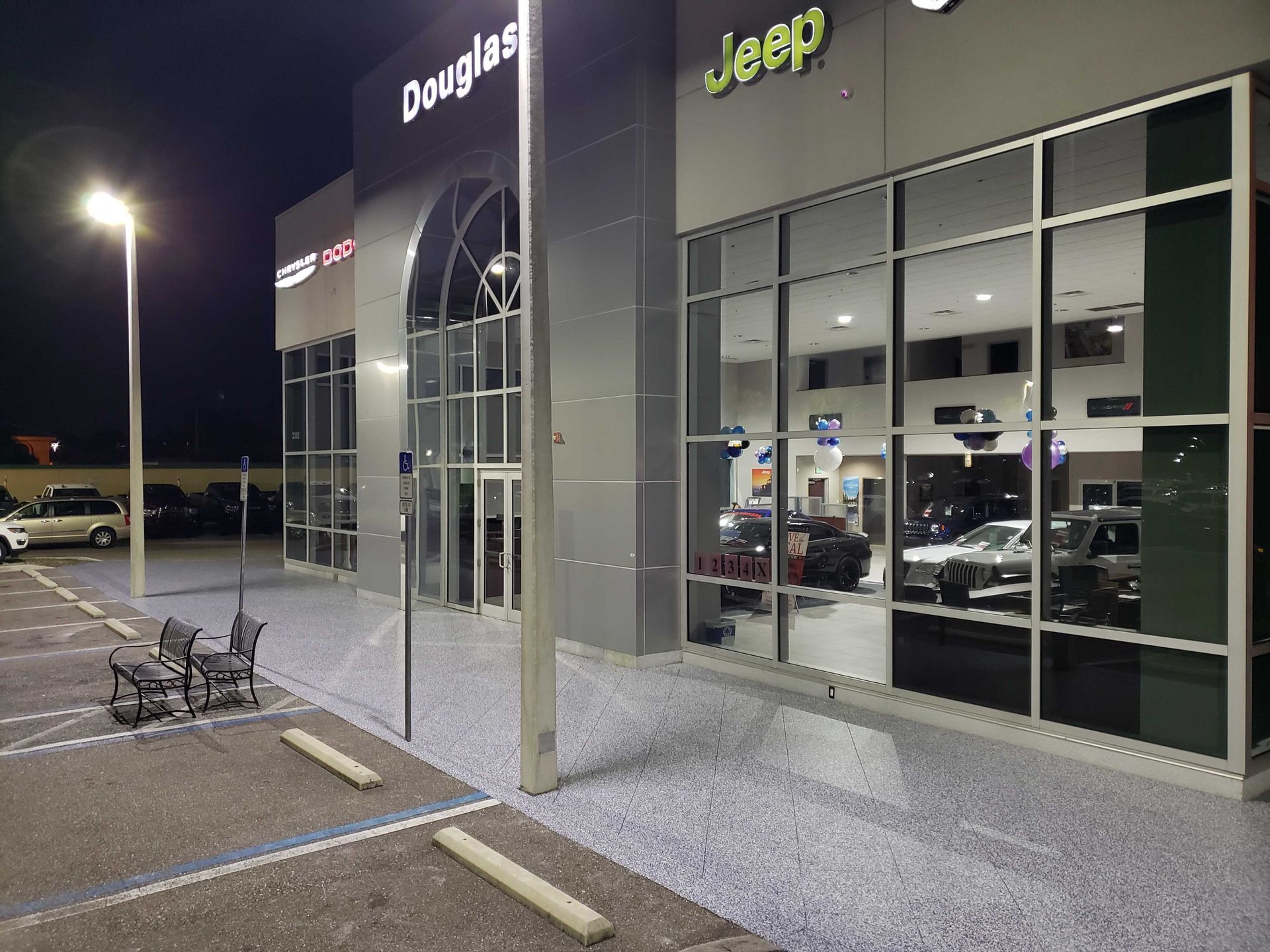 Nighttime view of a Douglas Jeep dealership. The building has large windows, revealing cars inside.