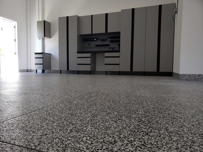 Garage with gray cabinets and speckled floor. The open door lets in bright light.