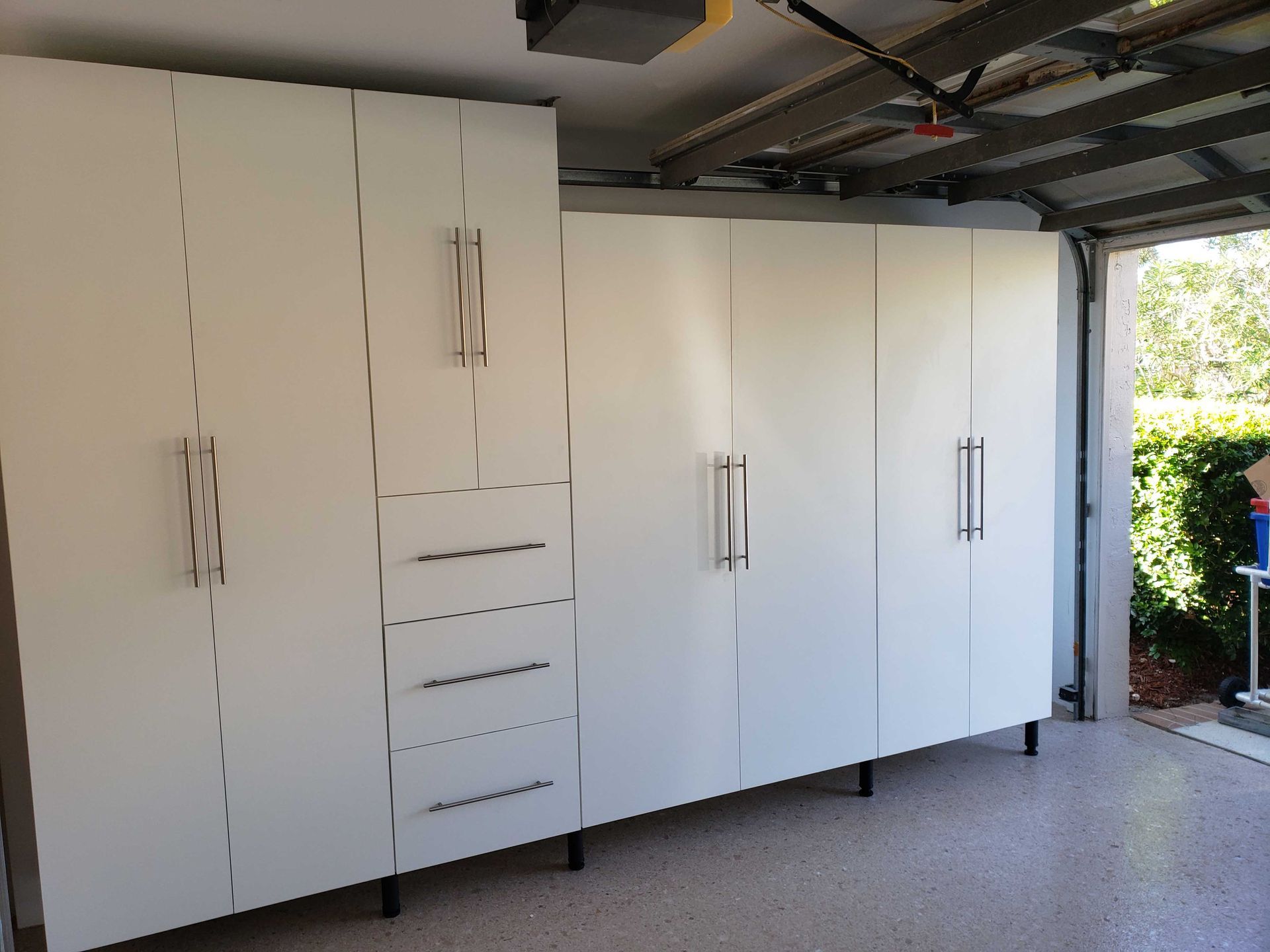 White garage storage cabinets with black handles and legs; mounted on speckled floor.