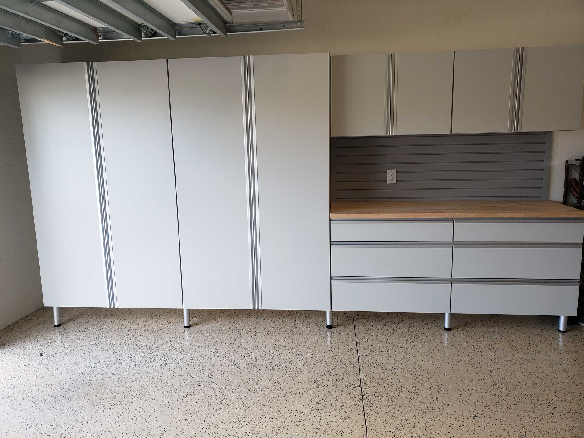 Garage storage cabinets; white with silver accents, a wooden countertop, and a gray pegboard.