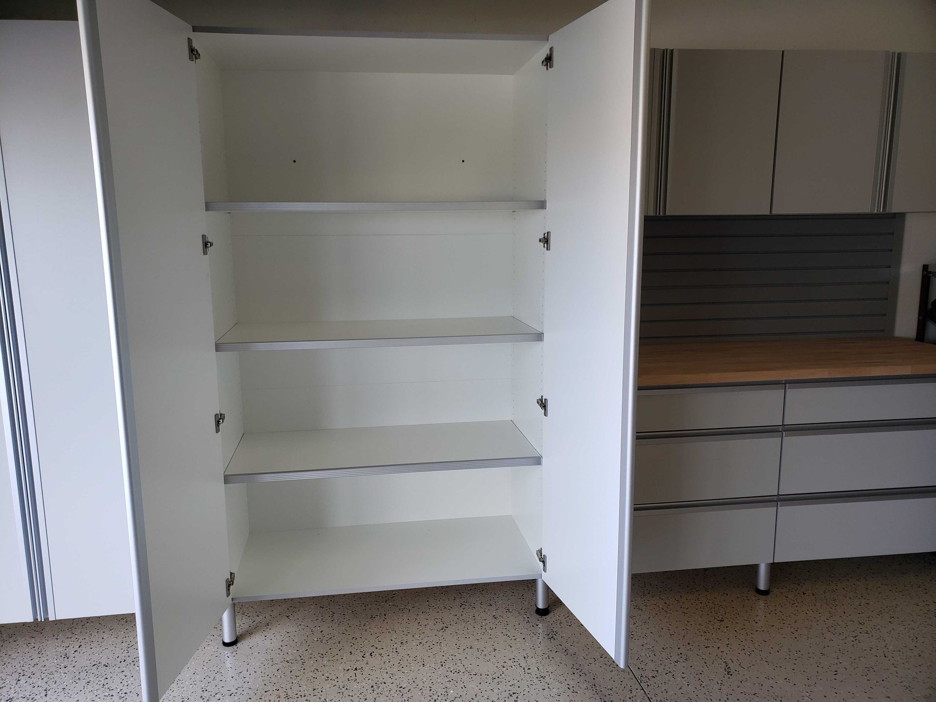 White storage cabinet with open doors, displaying three shelves, set in a garage.