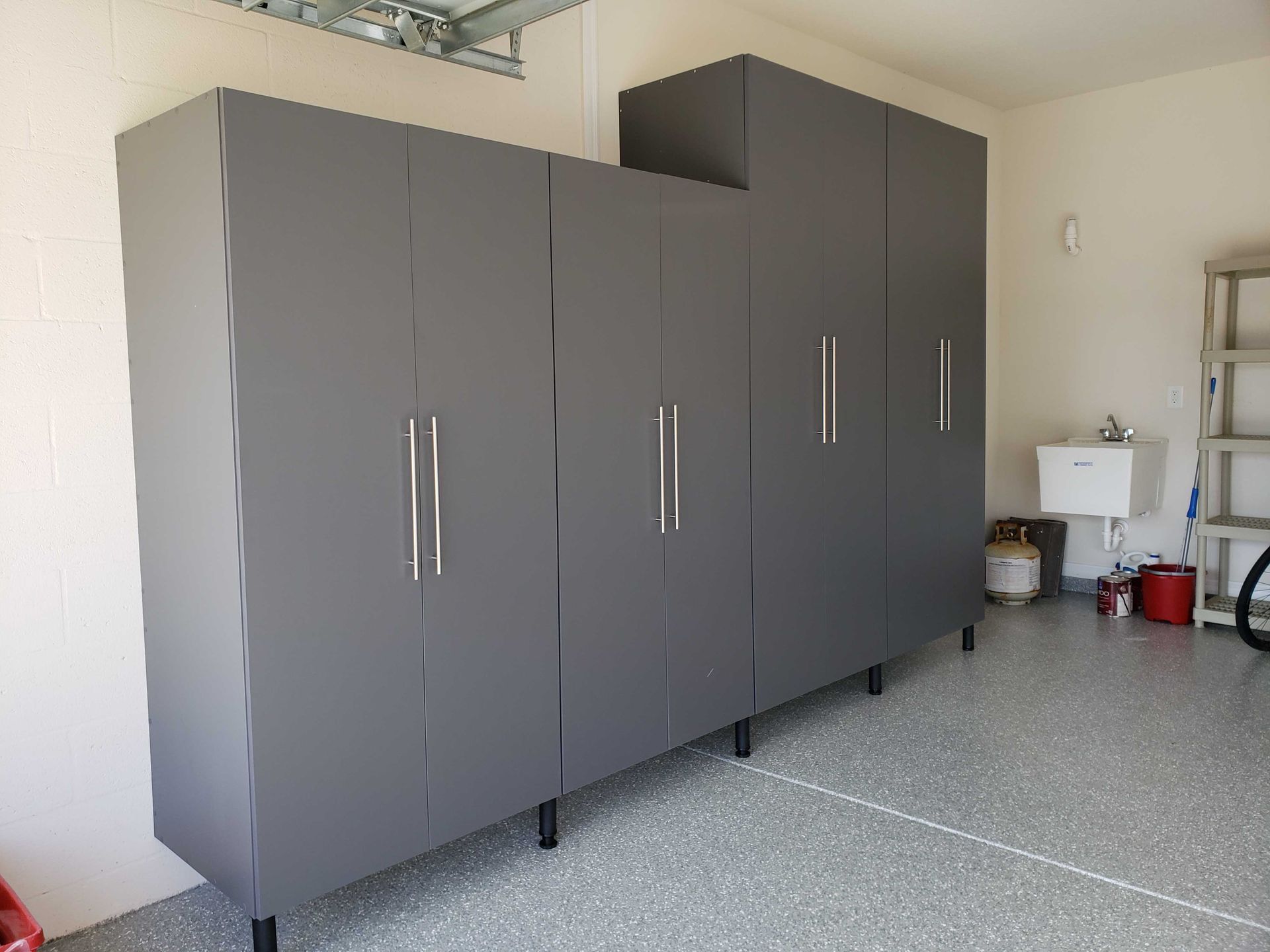 Gray garage cabinets against a white wall in a garage with a speckled floor.