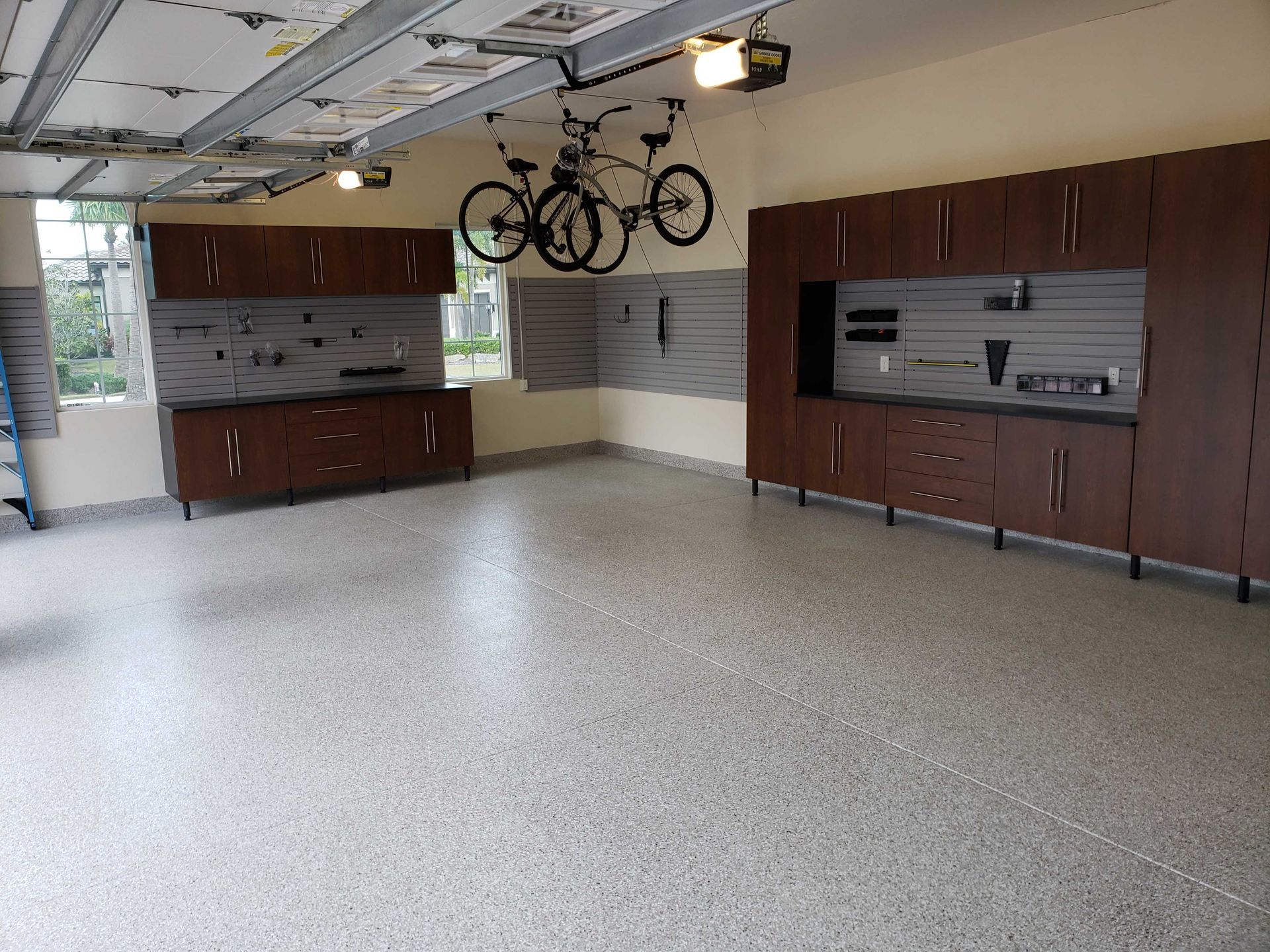 Garage with dark wood cabinets, gray walls, speckled floor, bikes hanging.