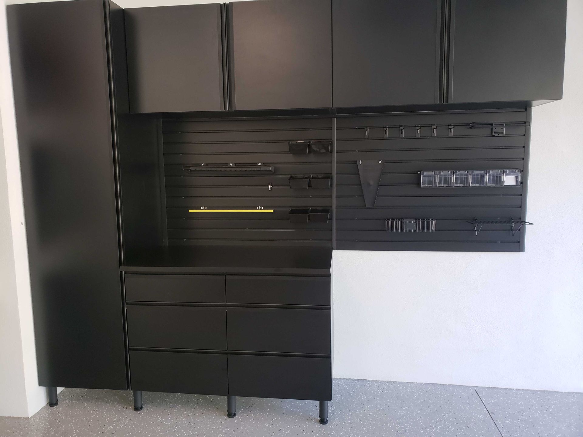 Black garage storage cabinets and tool rack against a white wall and gray floor.