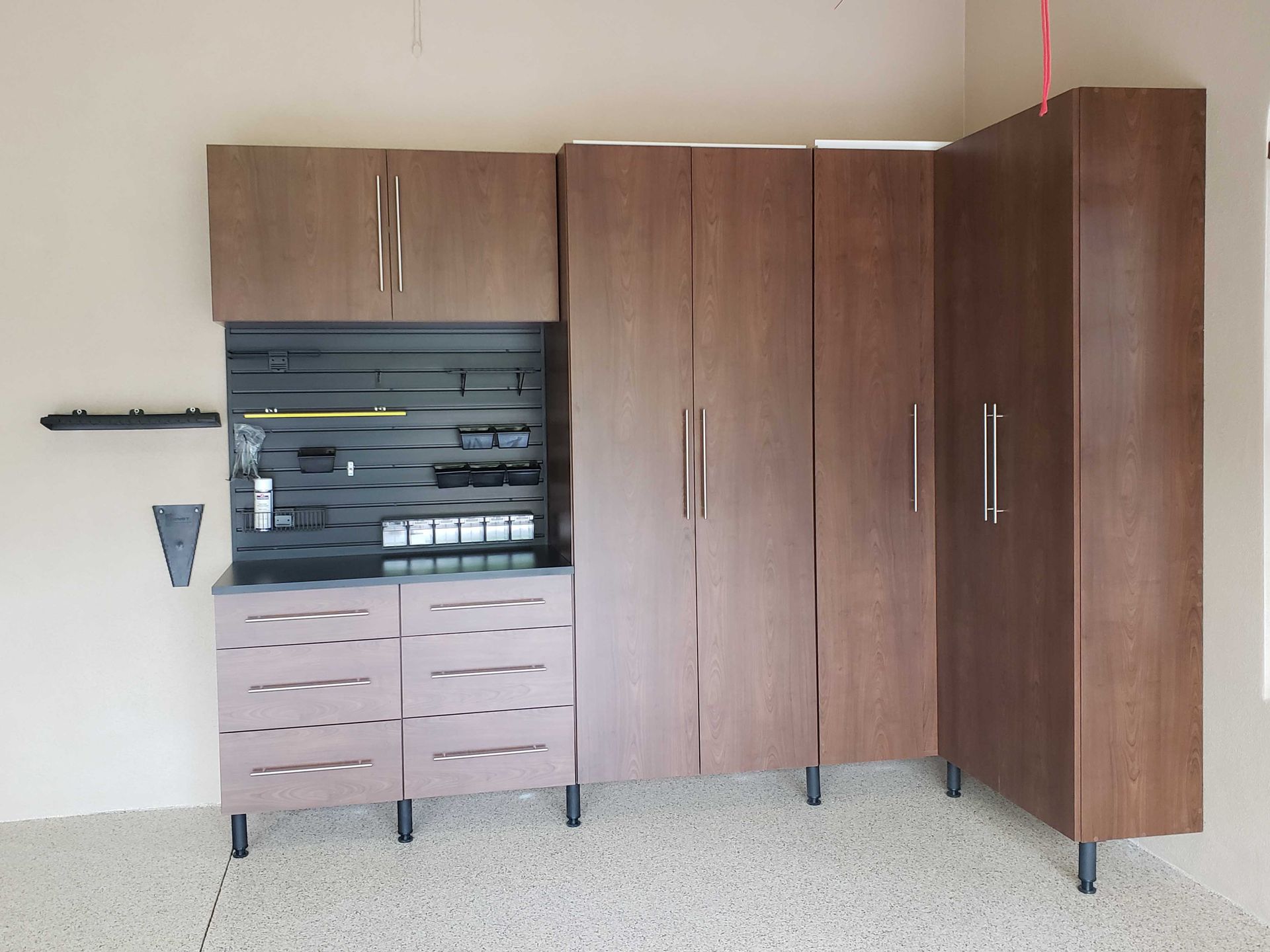 Garage storage cabinets, brown wood finish. Includes drawers, wall-mounted pegboard, and tall corner cabinet.