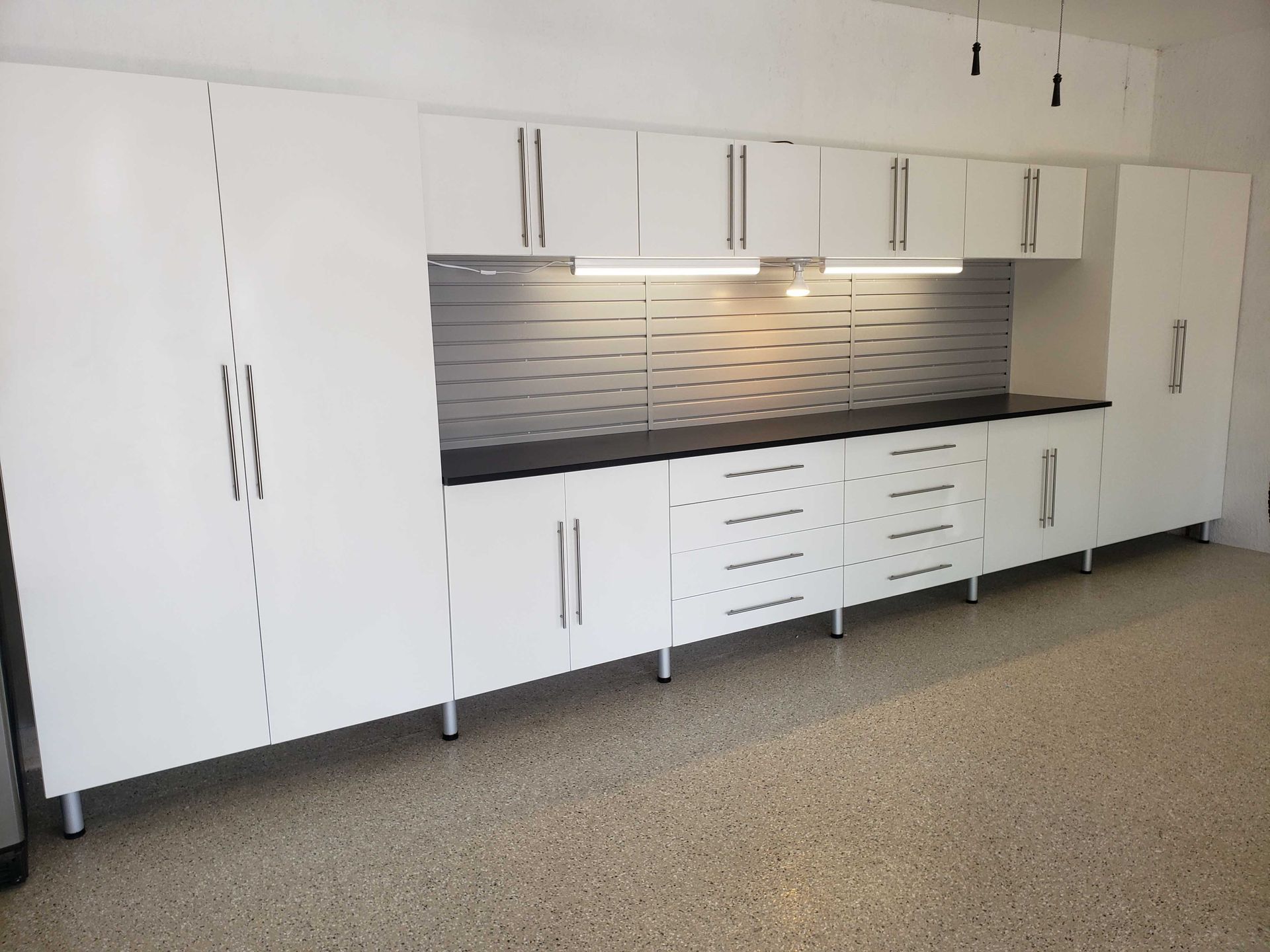 White garage cabinets with black countertop and gray backsplash.