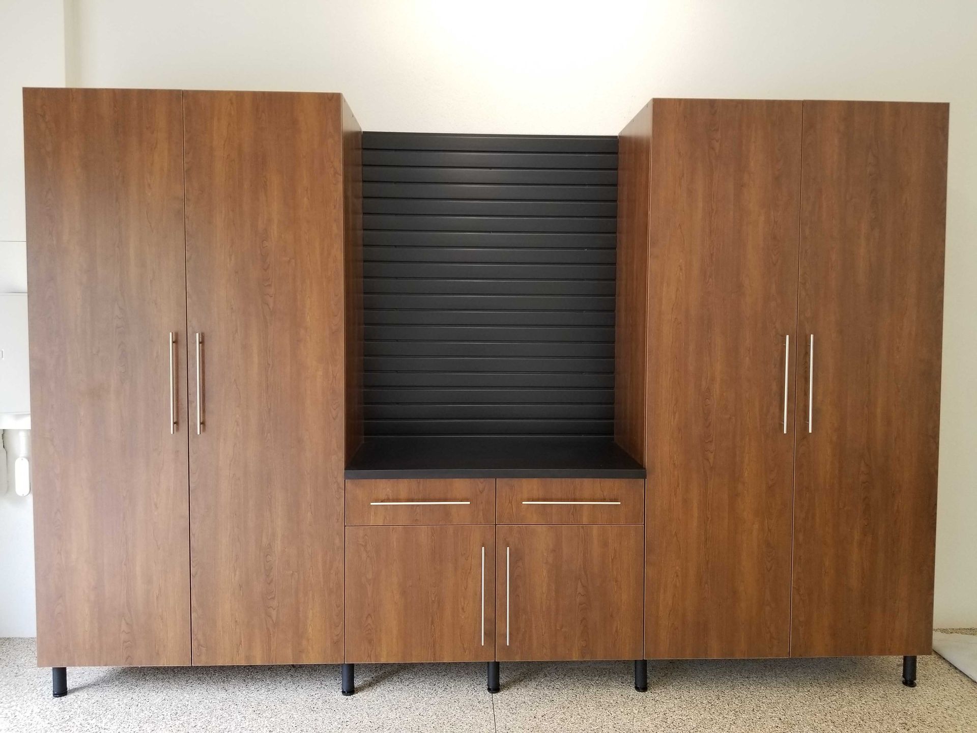 Wooden storage unit with dark cabinets, a black panel backdrop, and two lower drawers.