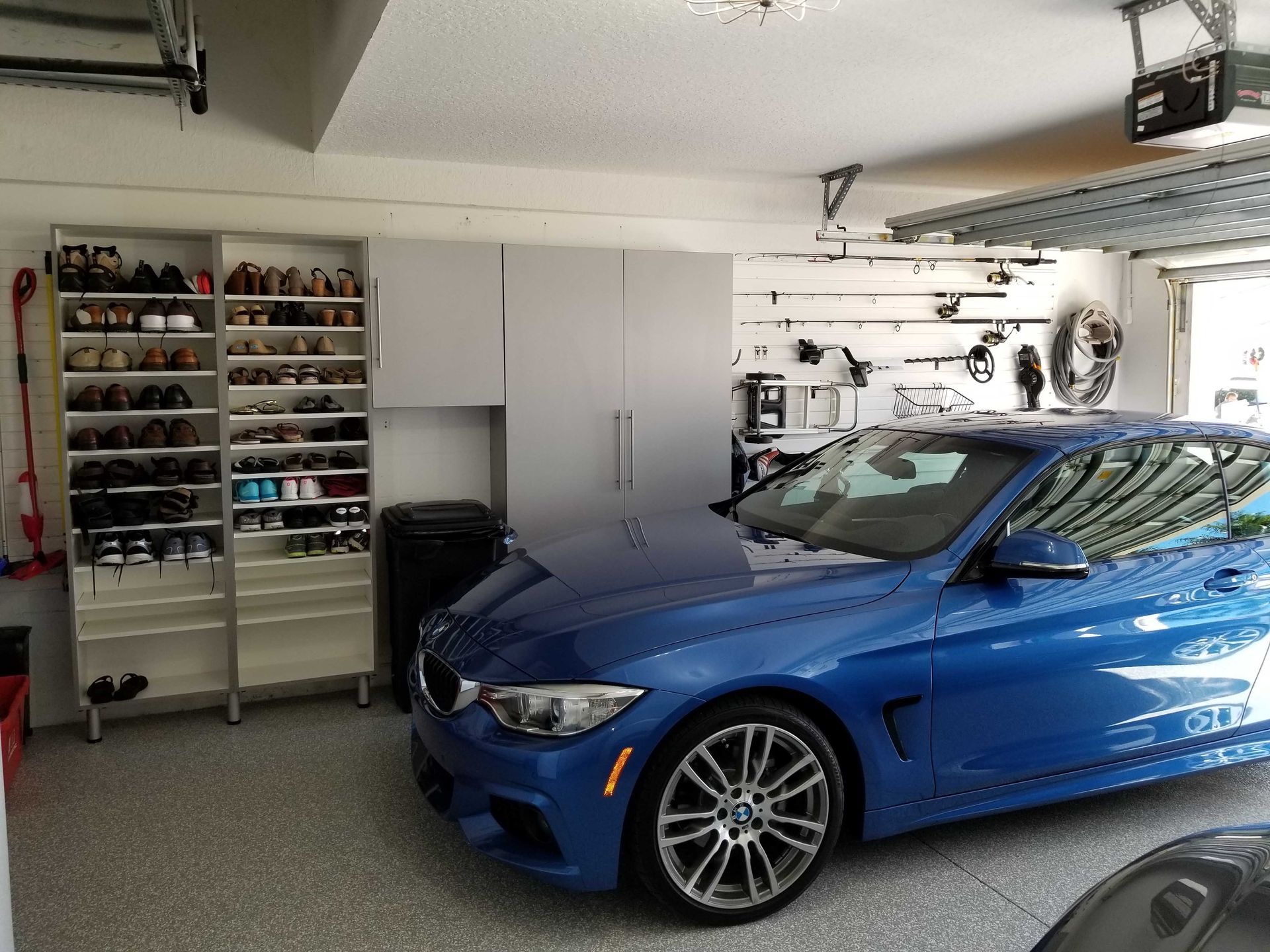 Blue BMW car parked in a tidy garage with organized storage and shoe rack.