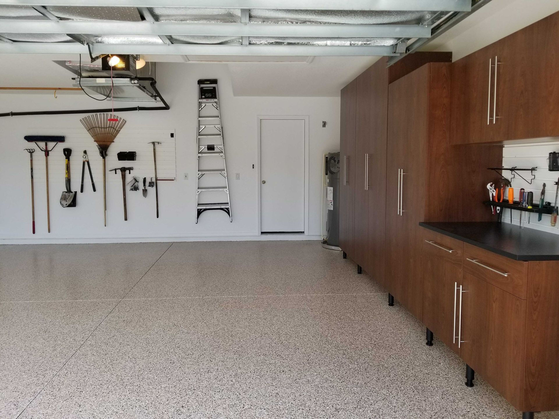 Garage with brown cabinets, tools on the wall, and speckled floor.