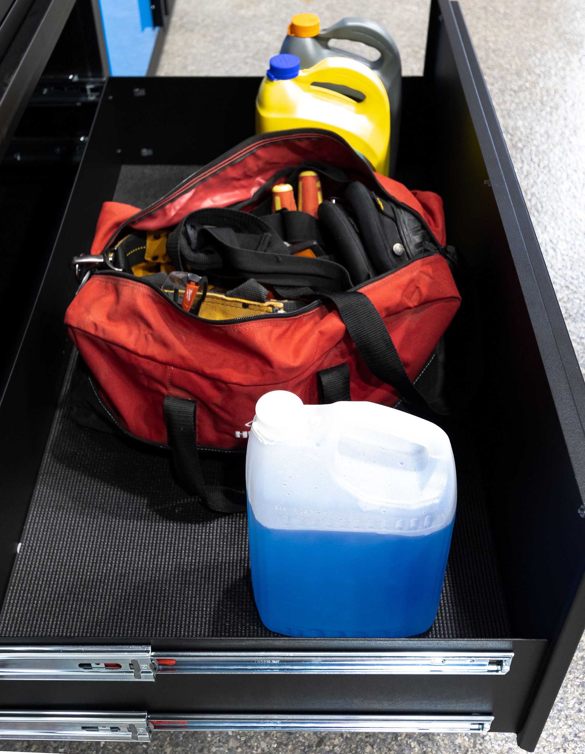 Open black drawer with a red tool bag, blue and yellow fluid containers.