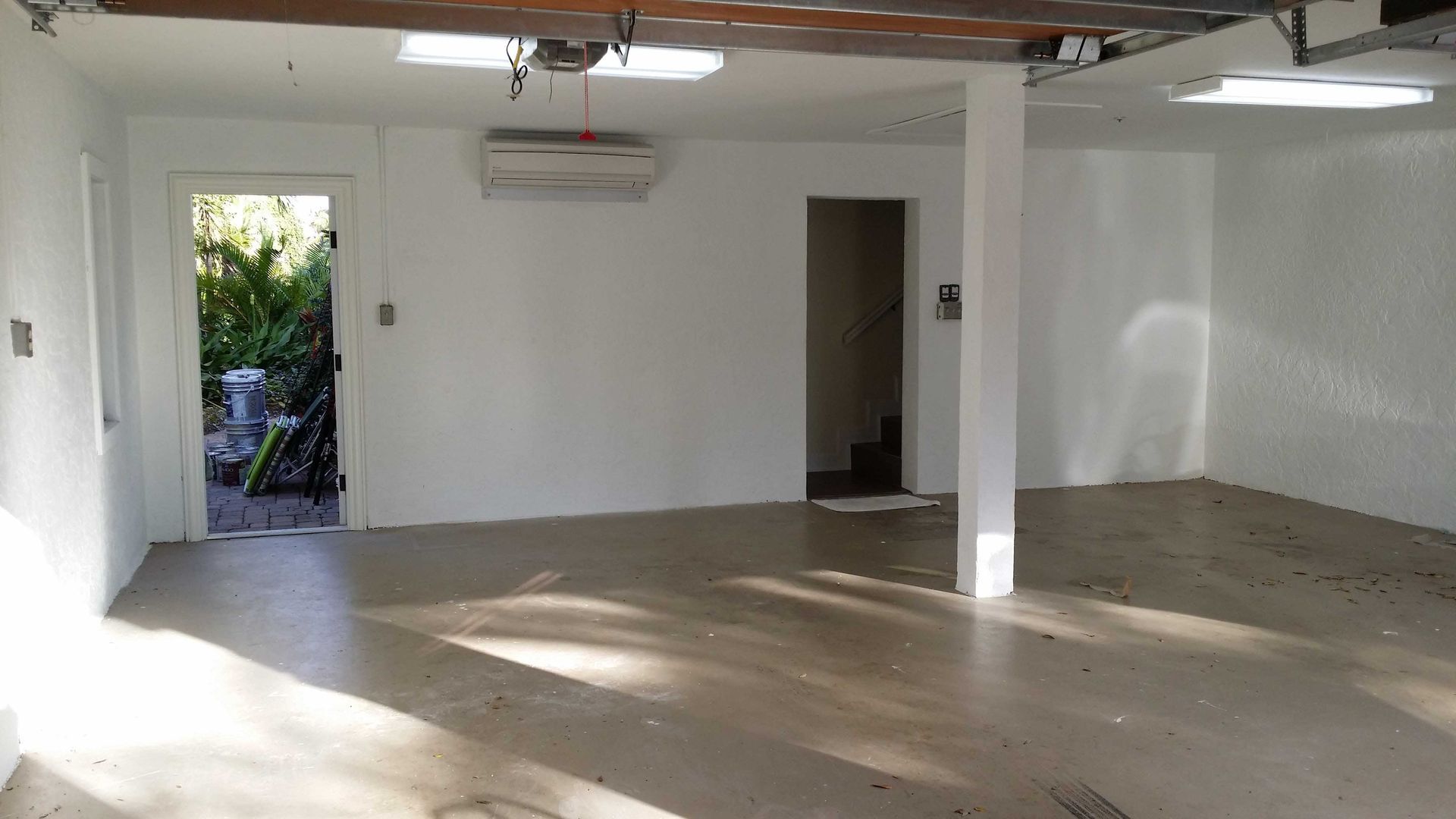 Empty, white-walled garage with concrete floor, door to outside, and a central support column.