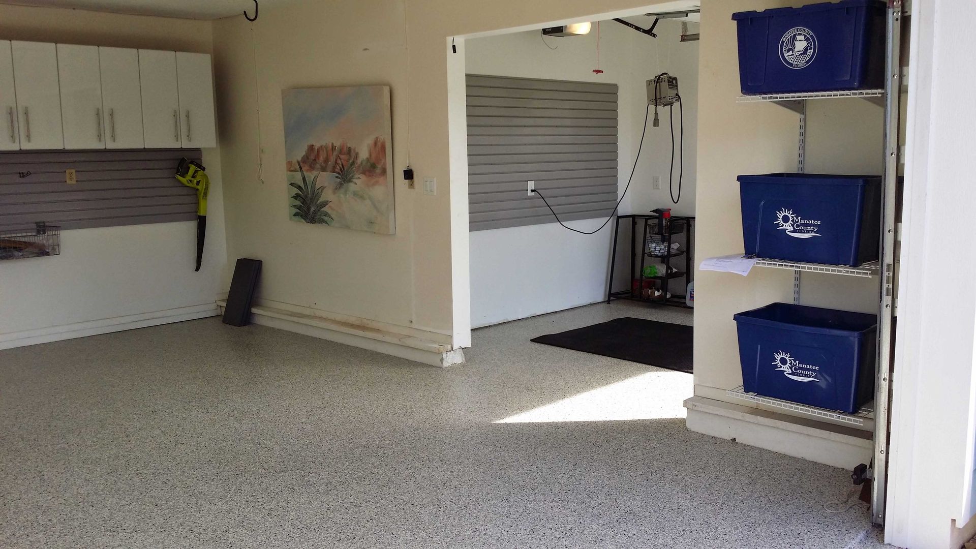 A clean garage with white cabinets, speckled floor, art, and blue bins on shelves.