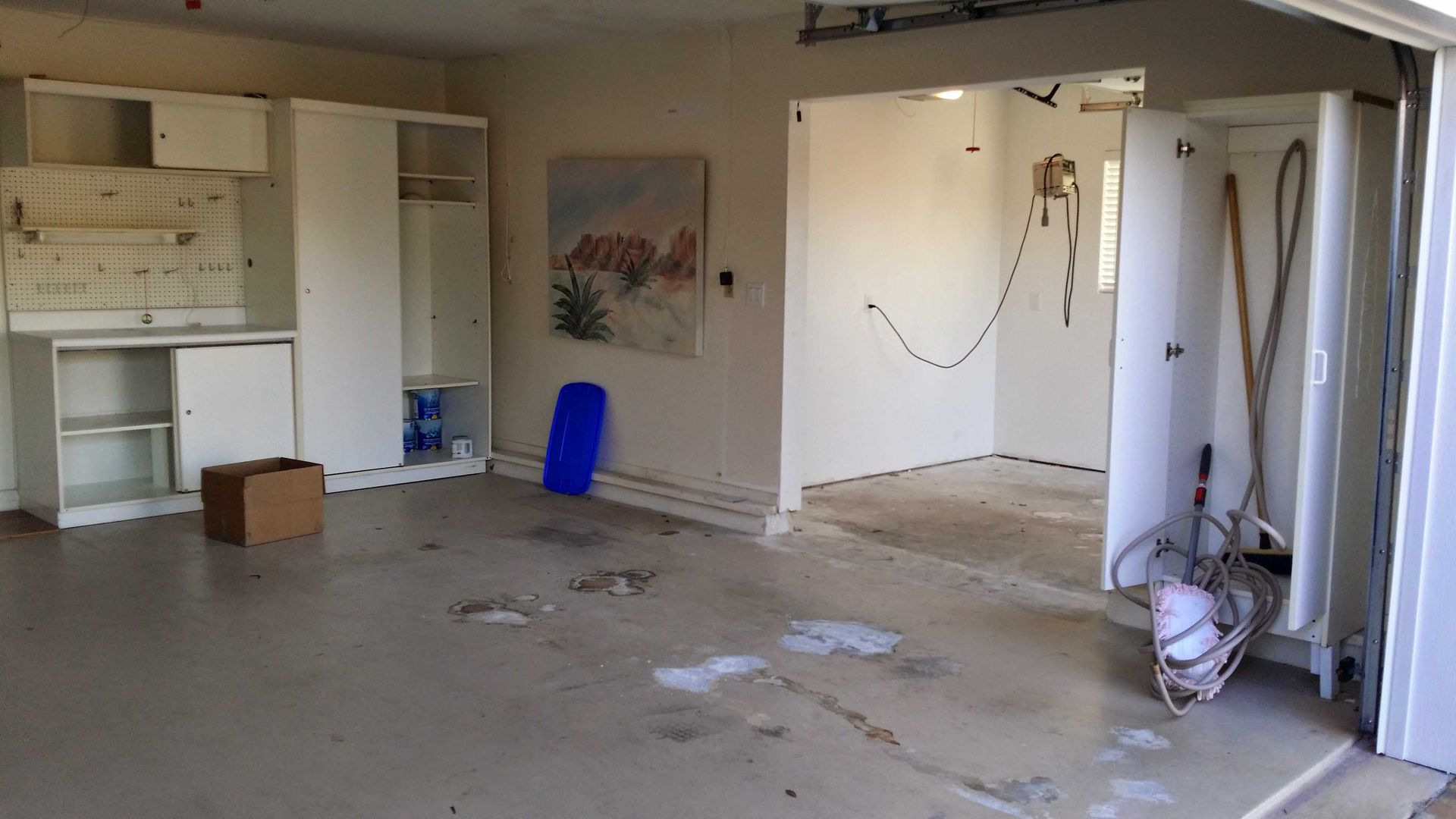 Empty garage with white cabinets, paint splatters on the walls, and a partially open door.