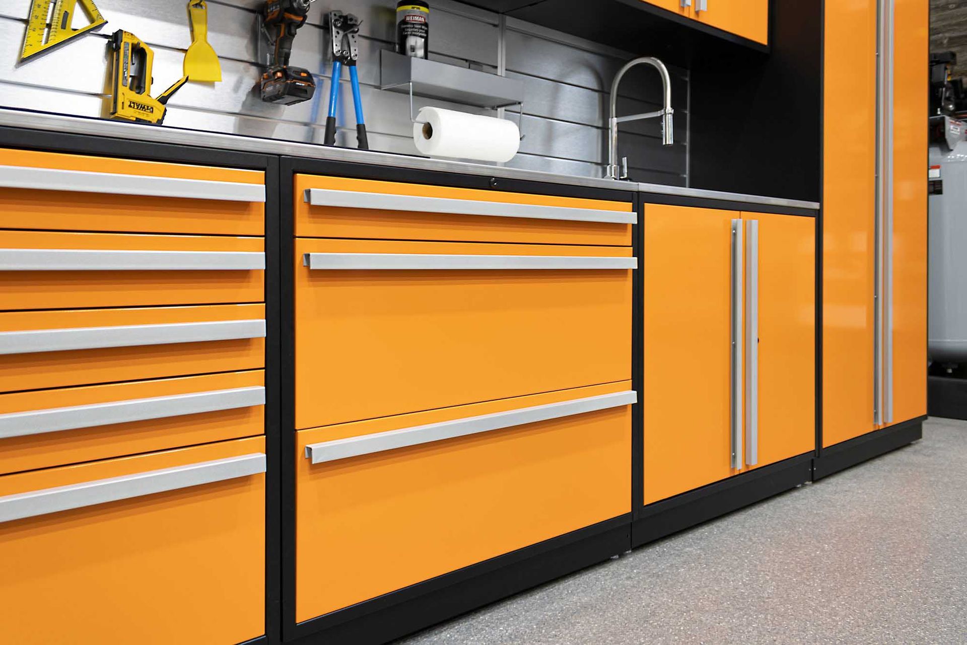 Orange garage cabinets with silver handles, tools on a wall, and a sink.