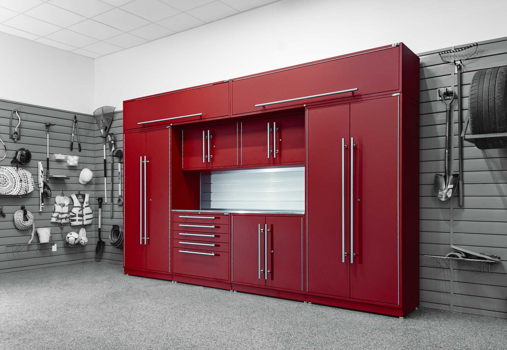 Red garage storage cabinets against a gray wall with tools and a tire.