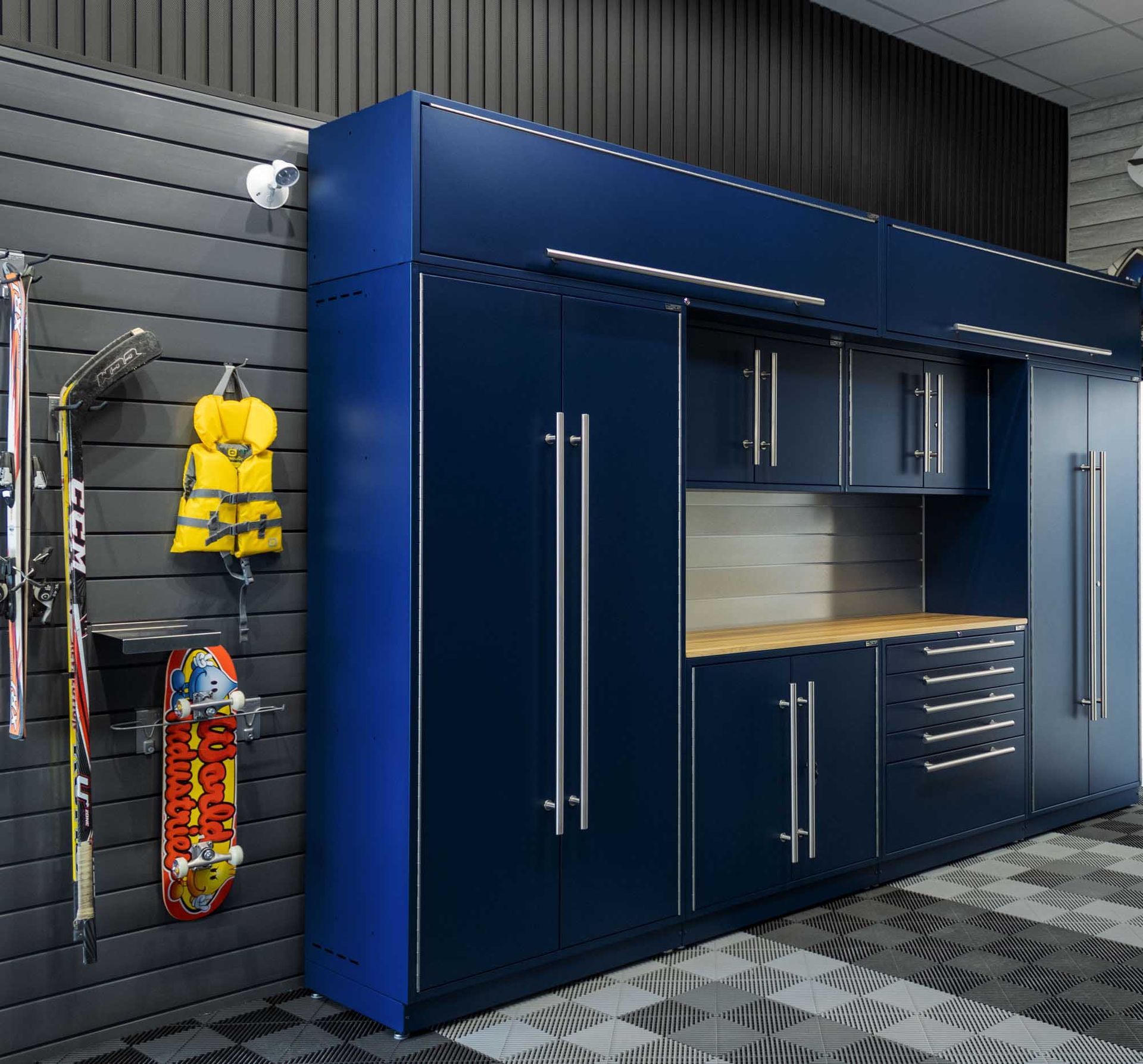 Blue garage storage cabinets with a workbench, and a wall rack with skis, a life jacket, and a skateboard.