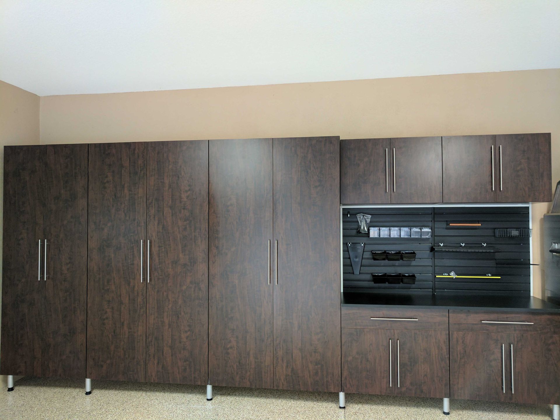 Brown storage cabinets with silver handles against a tan wall, with some open shelves and appliances.