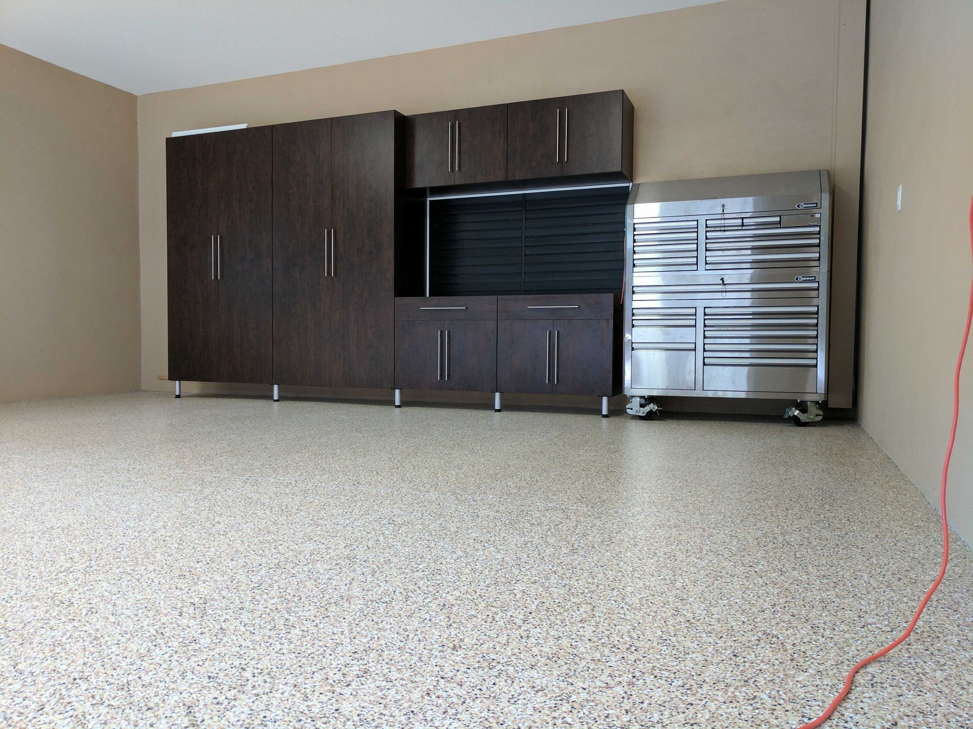 Garage with dark wood cabinets, silver toolbox, and speckled floor.