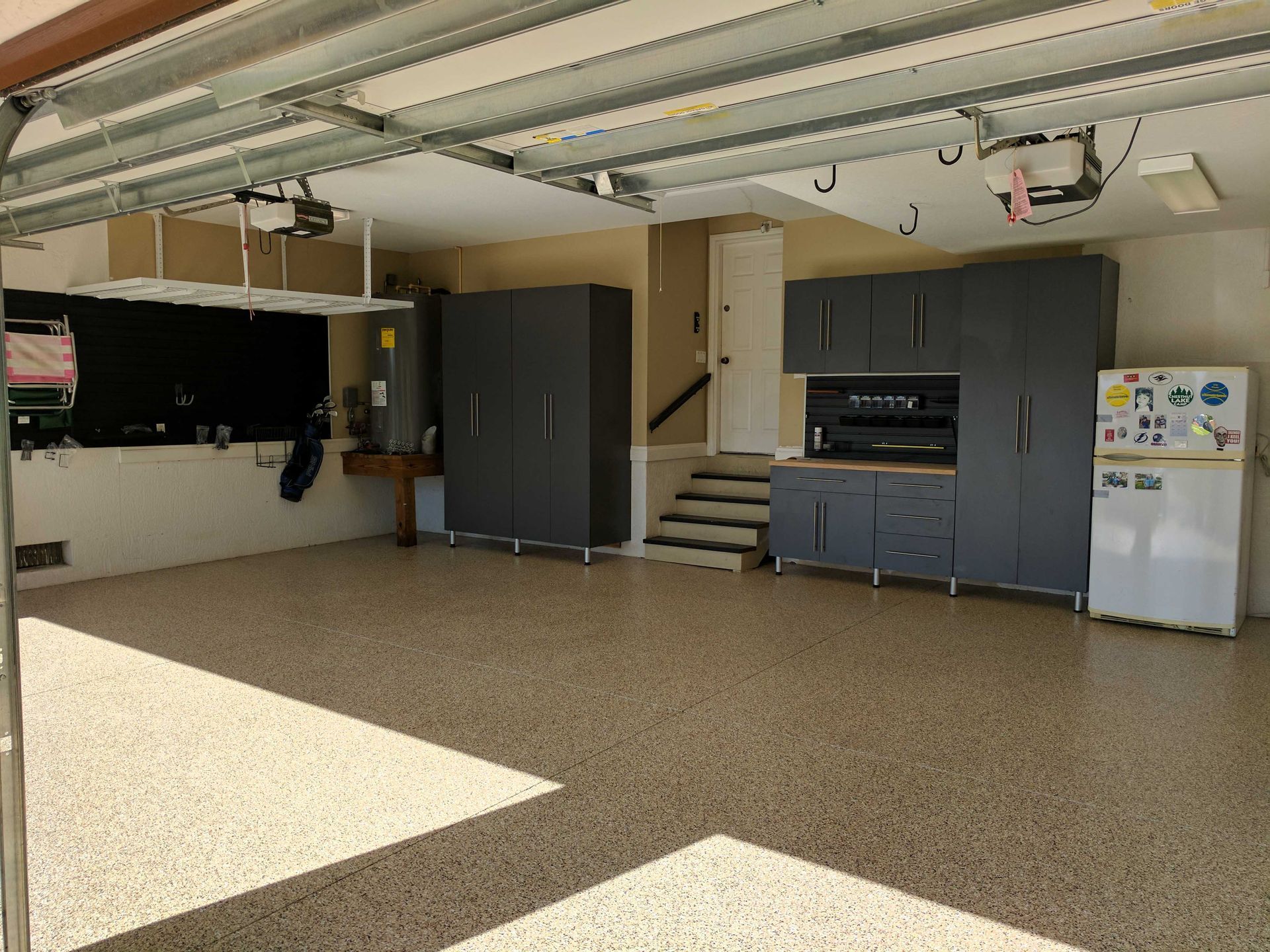 Spacious garage with grey cabinets, speckled floor, and a white refrigerator.
