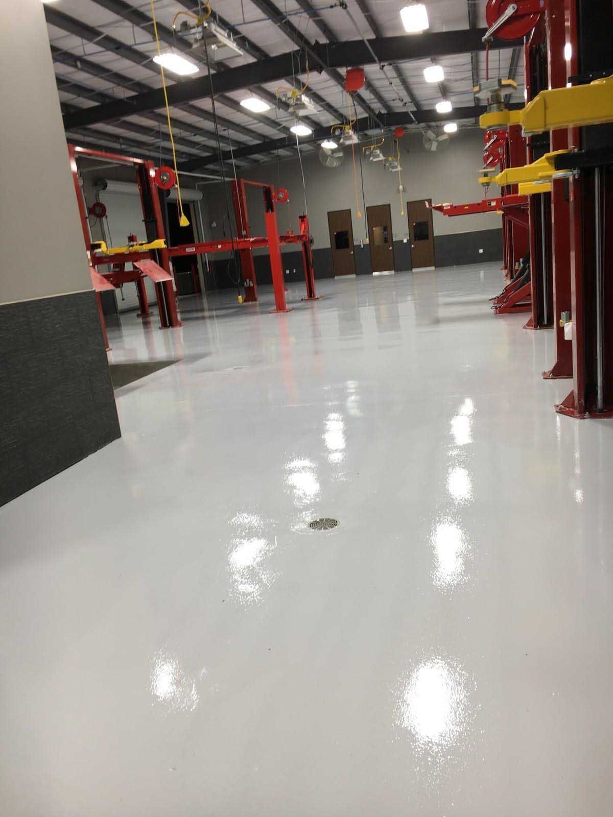 Bright white floor in an auto repair shop, red lifts and equipment, and an open ceiling.