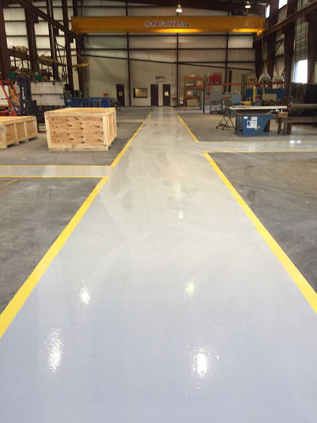 Factory floor, gray and yellow painted lines, wooden crates, overhead crane, industrial setting.