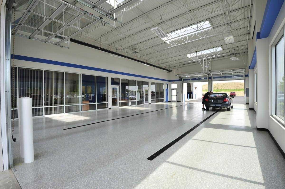 Wide, bright car dealership interior with a car entering, large windows, and a long central black line.