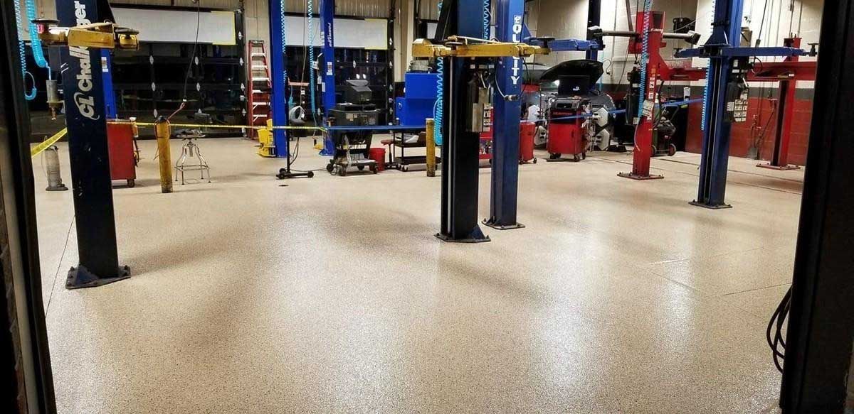 Inside a brightly lit auto repair shop with multiple vehicle lifts. The floor has a speckled pattern.