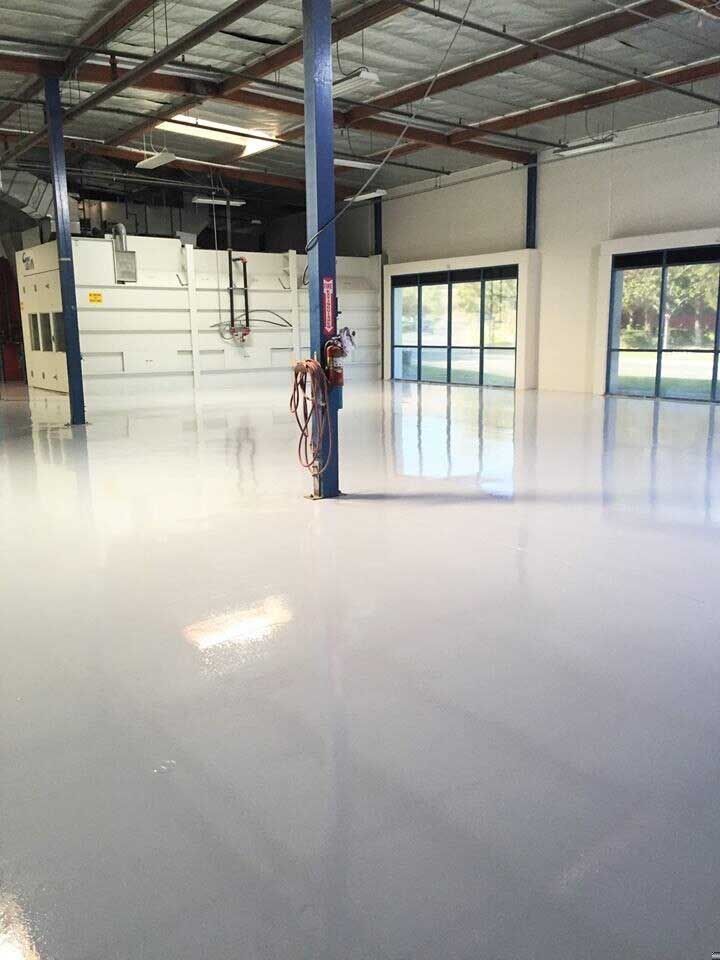 Shiny, light-grey epoxy floor in a large, empty industrial space with a blue support column.